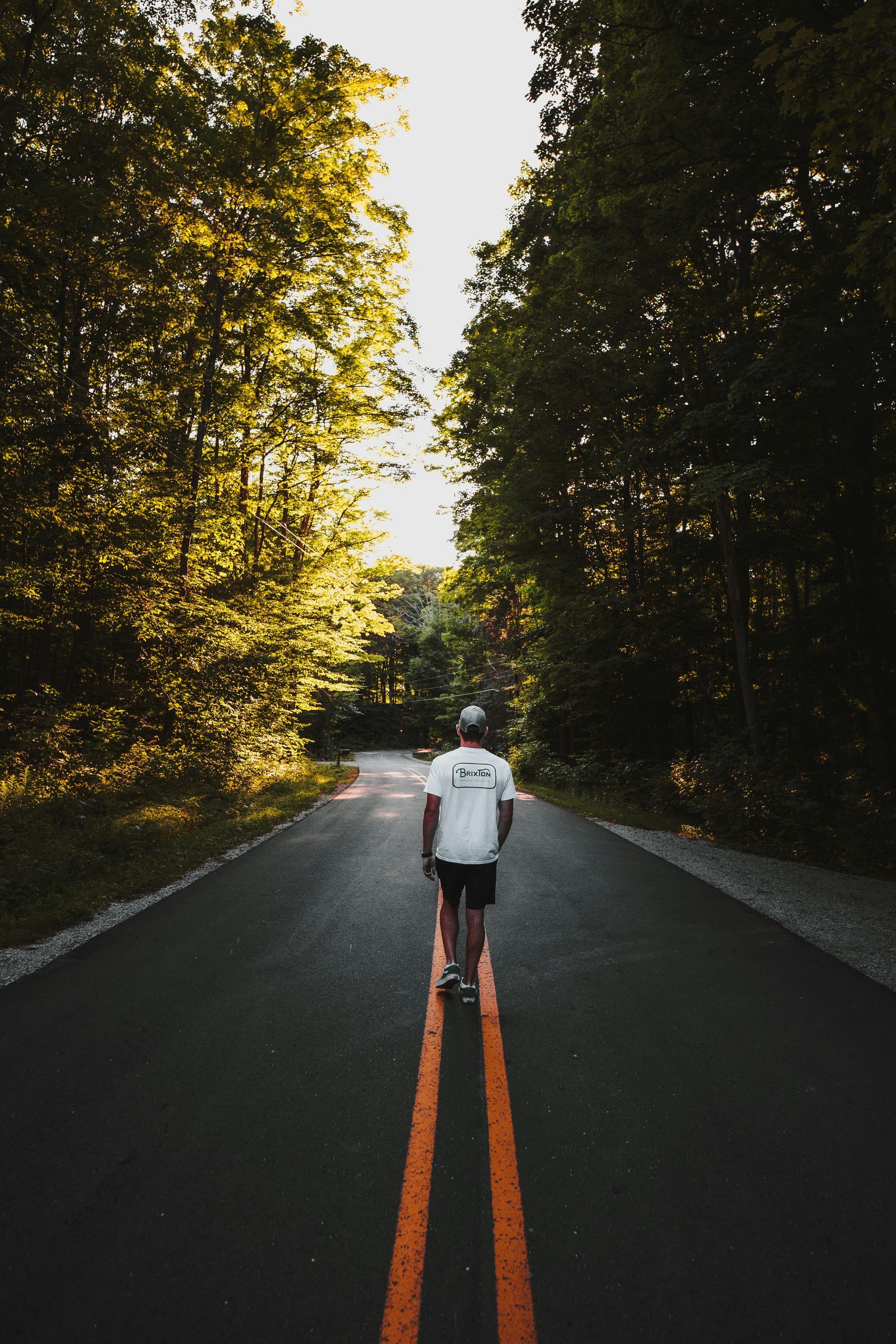 A man is walking down a road with trees on both sides.