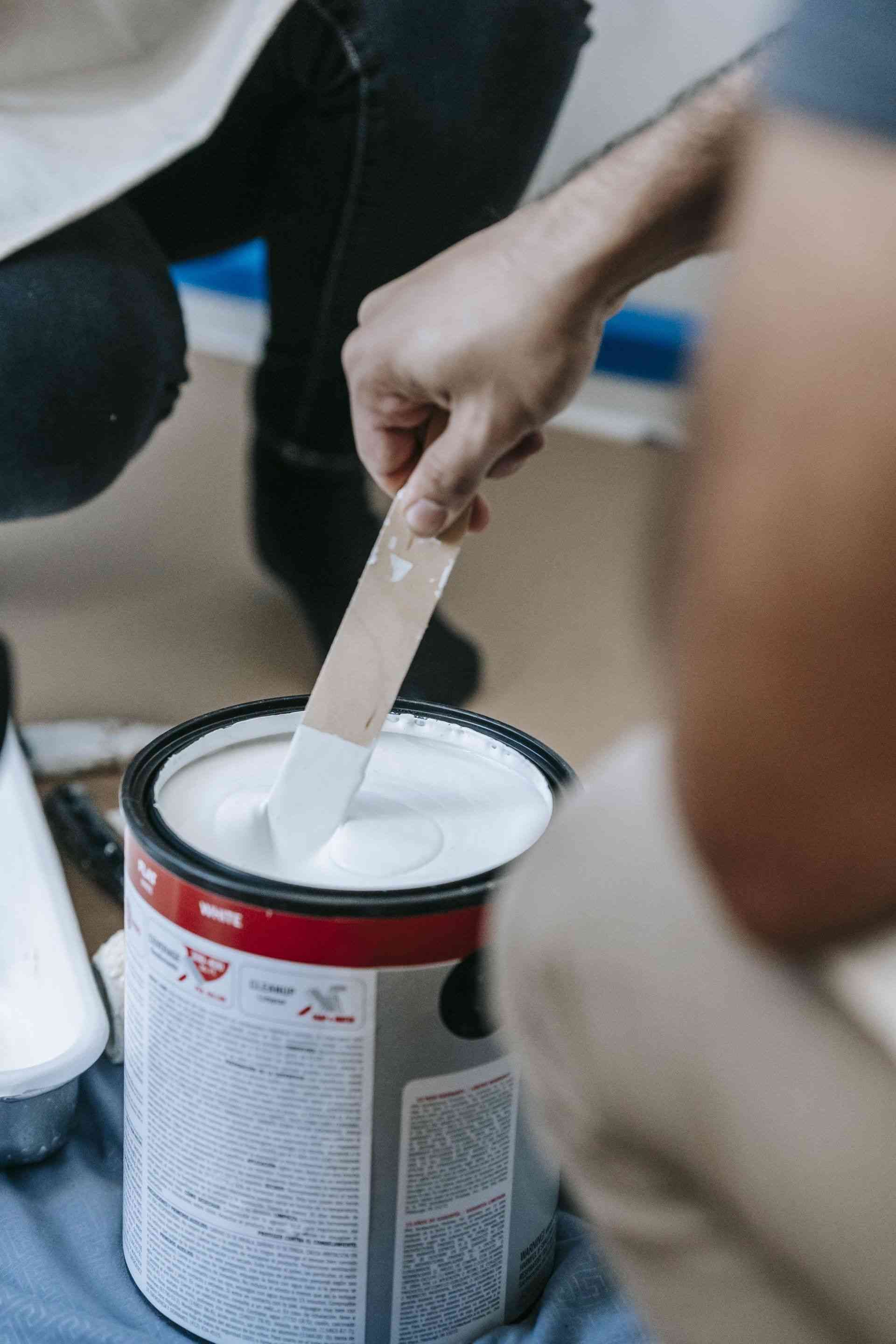 A person is mixing paint in a can with a brush.