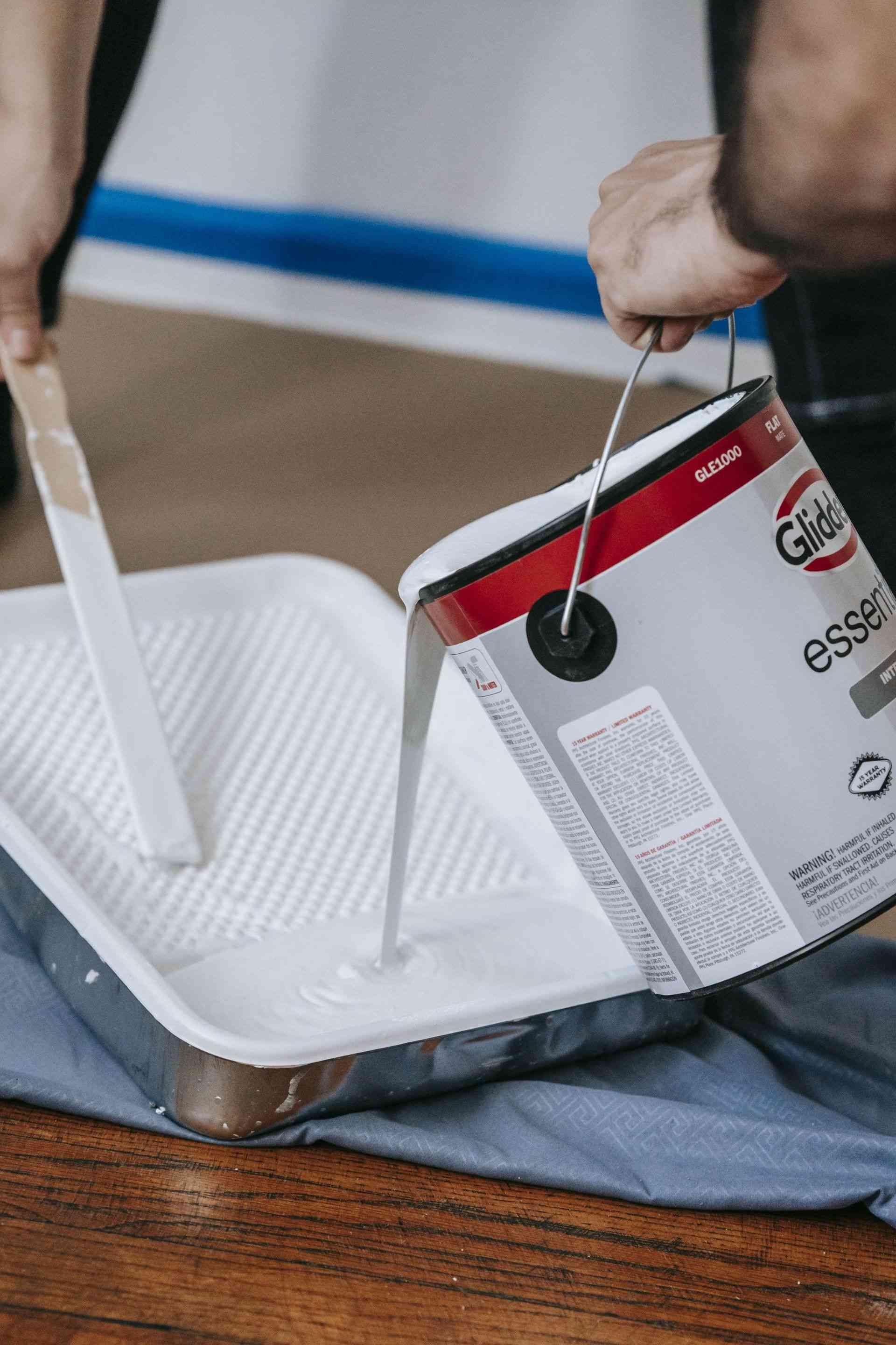 A person is pouring white paint into a paint tray.