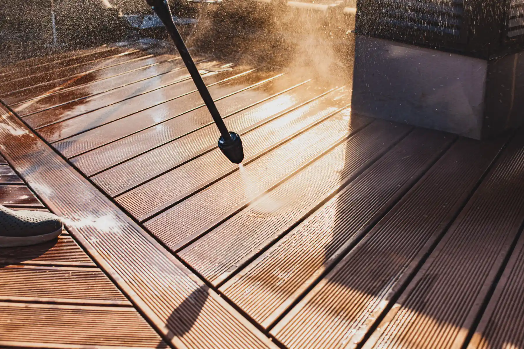 A person is cleaning a wooden deck with a high pressure washer.