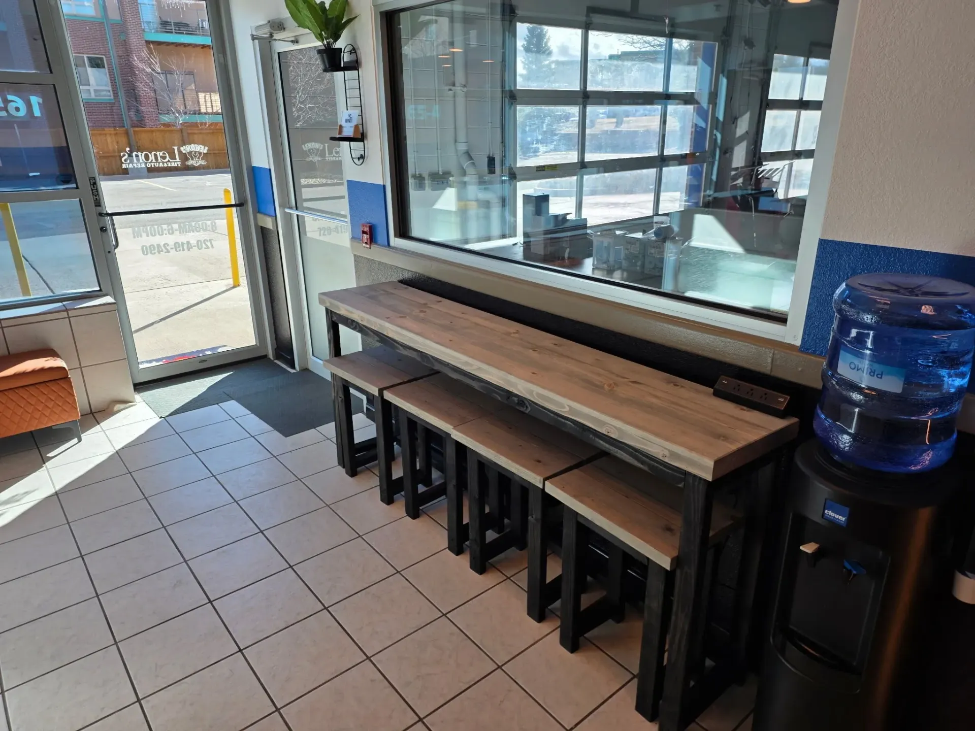 Interior of a business with a counter, stools, and water dispenser near a window. Sunlight streams in.