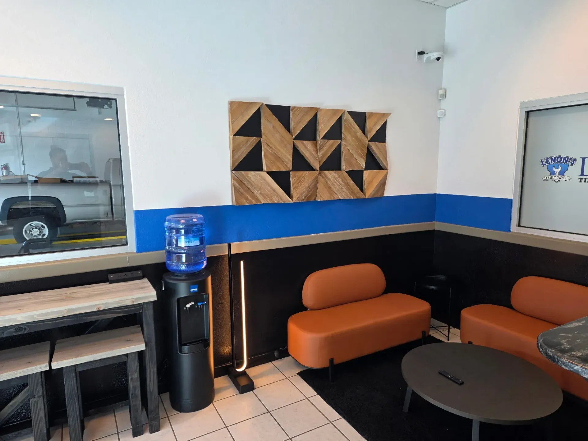 Waiting area with orange couches, black carpet, water cooler, and wooden wall art.