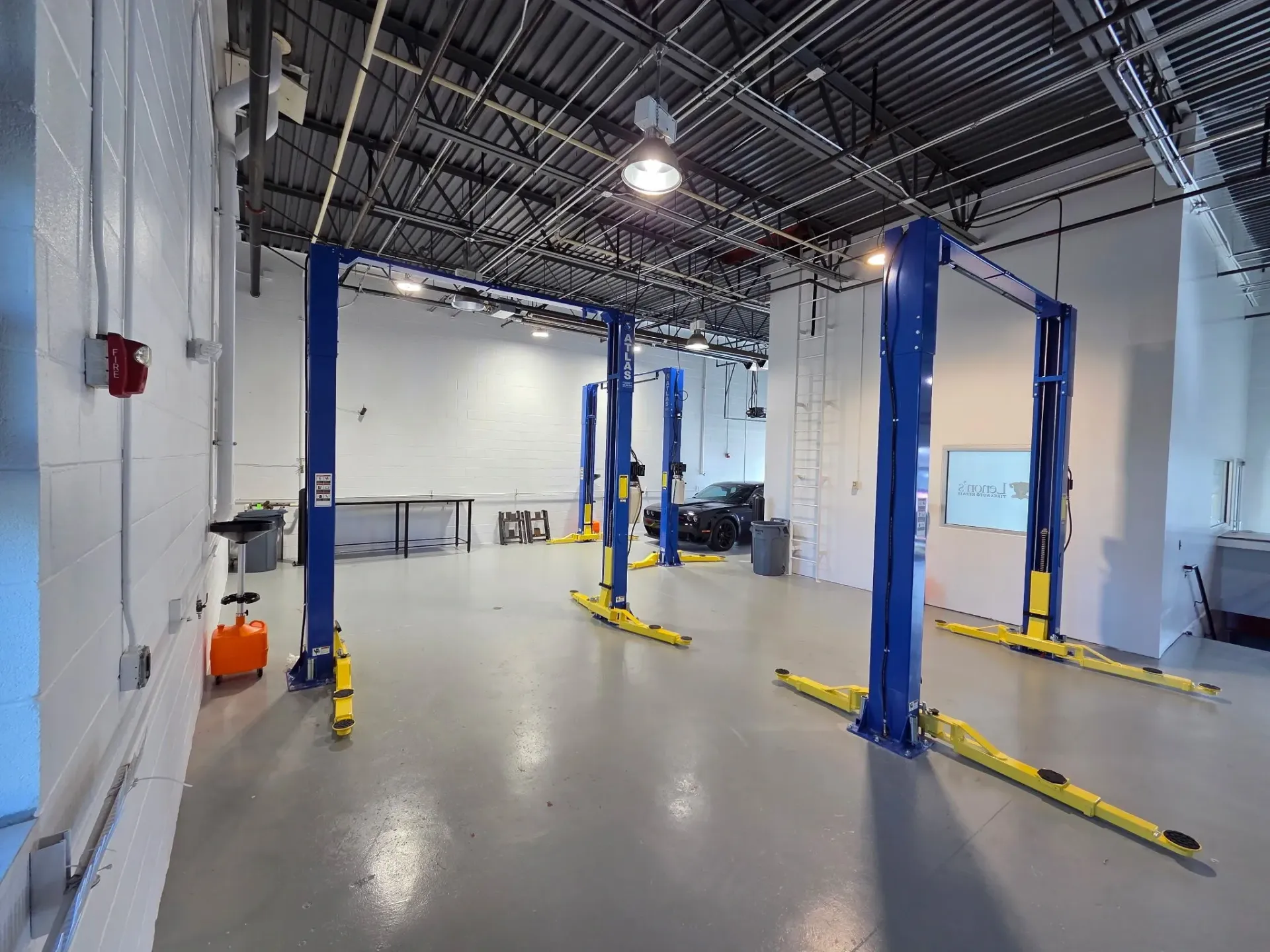 Automotive repair shop interior with several blue car lifts on a gray floor.