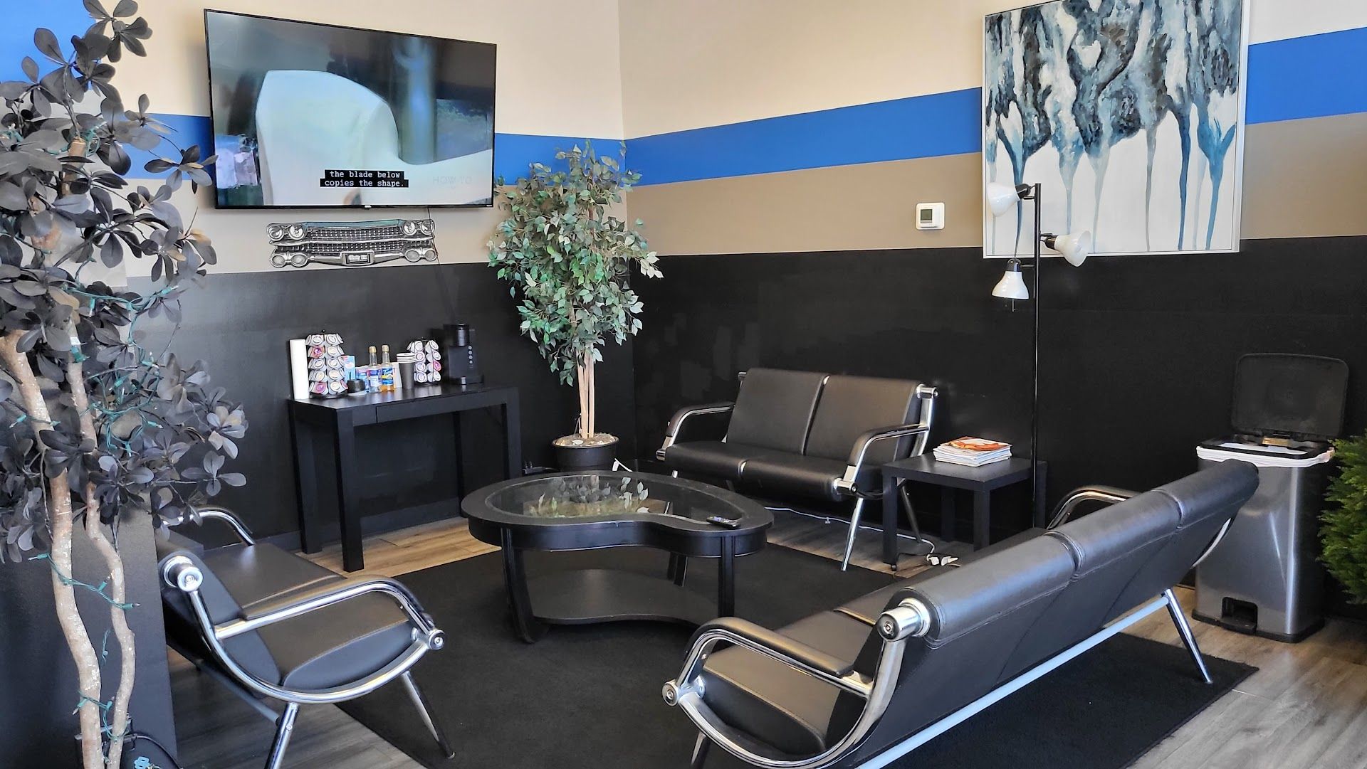 Lounge area with black furniture: sofas, chairs, table, TV, art, and a plant. Blue and gray wall accents. | Lenon's Tire & Auto Repair