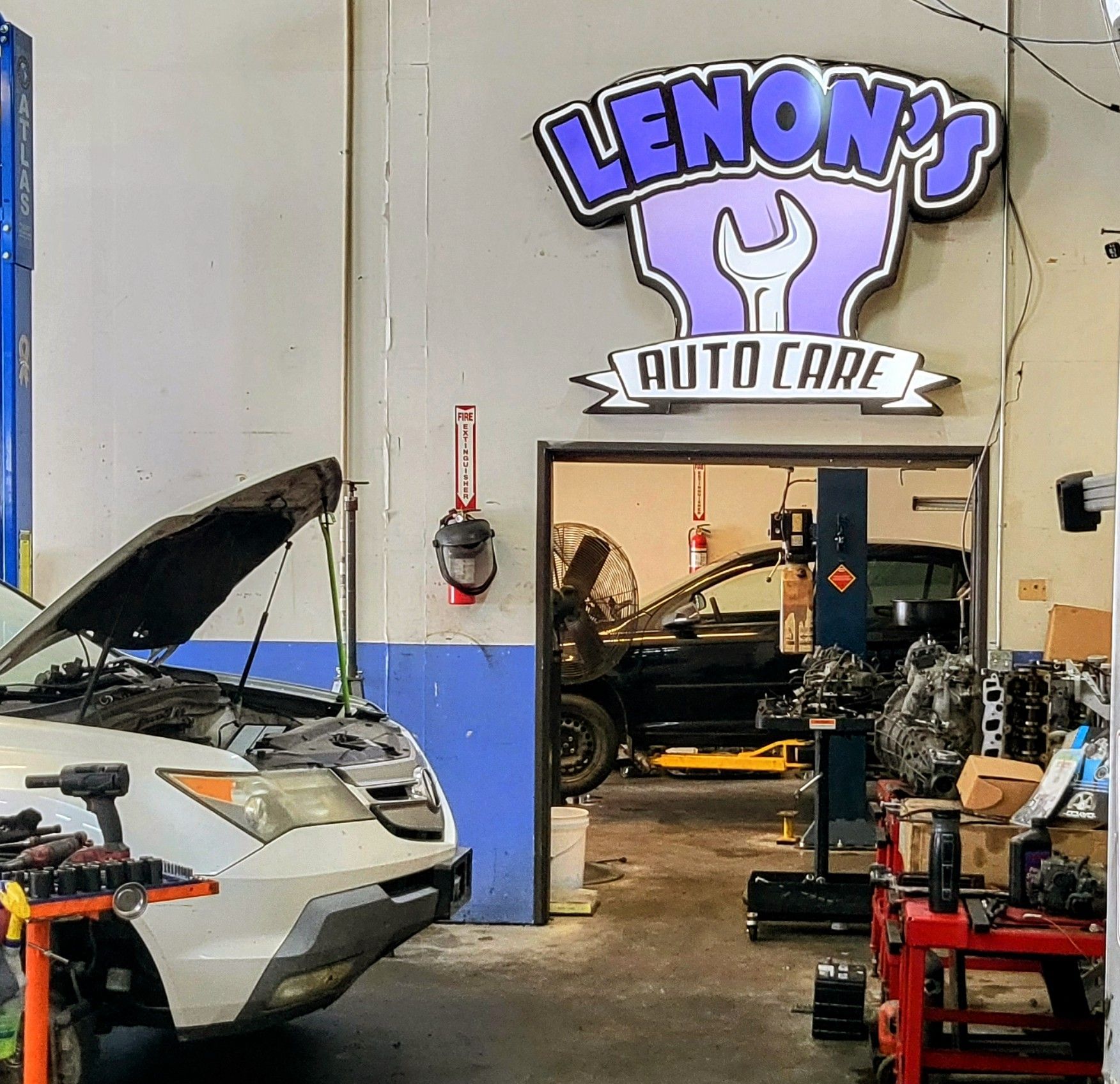 Interior of Lenon's Auto Care garage. A car is under repair with its hood up. A sign above the doorway reads
