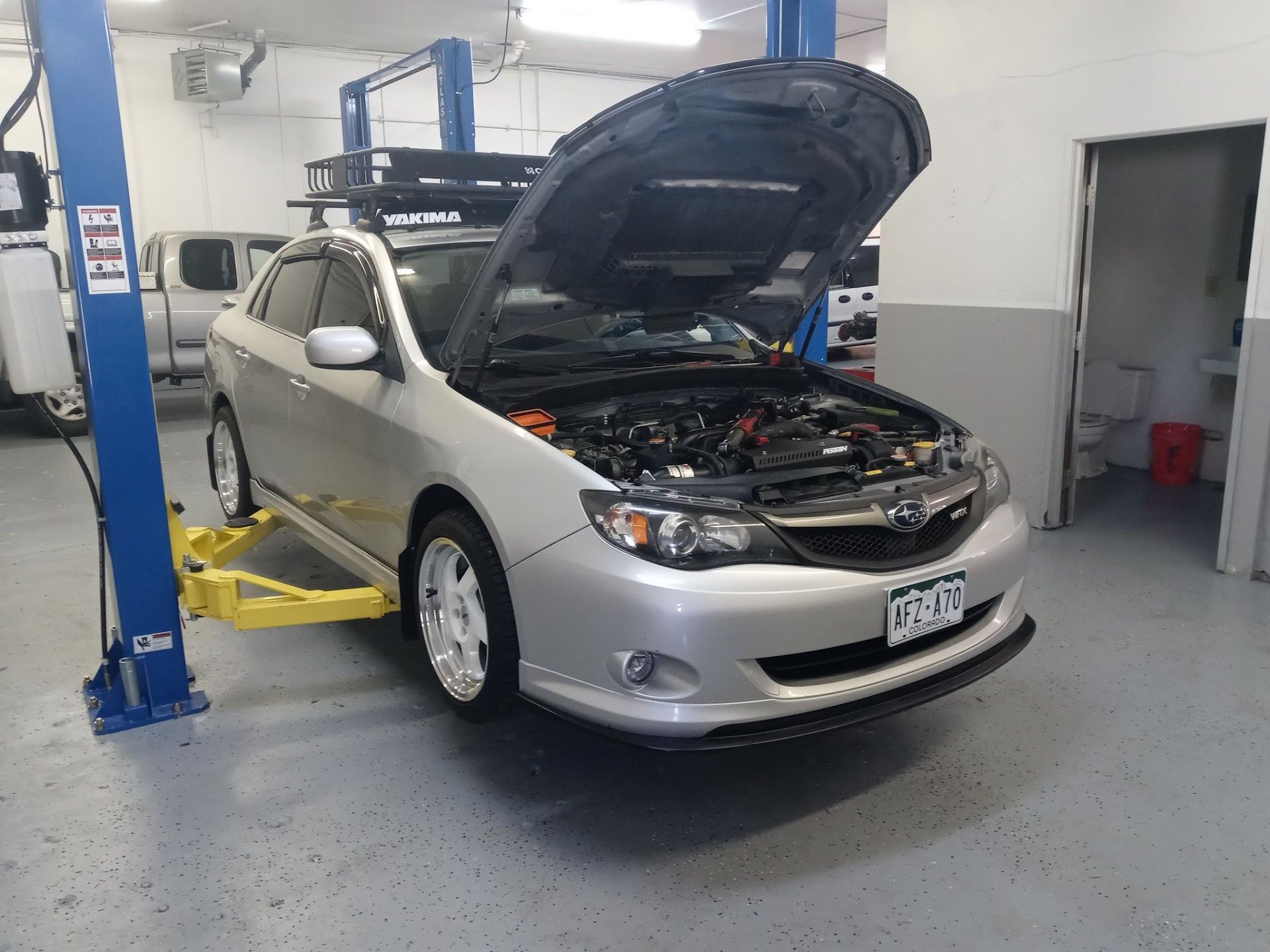 Silver car with open hood on a lift inside a mechanic's shop. | Lenon's Tire & Auto Repair
