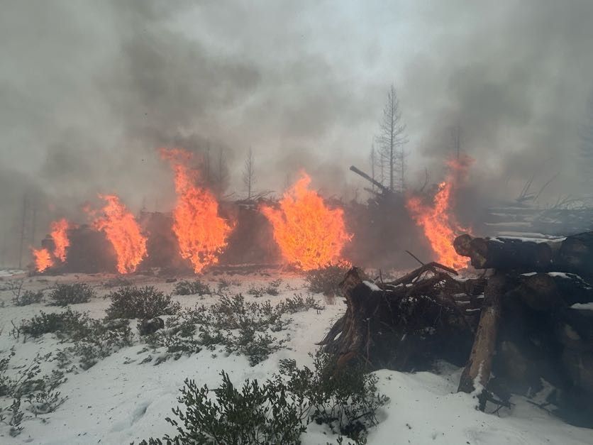 Wildfire burning through a snow-covered landscape with flames and smoke.