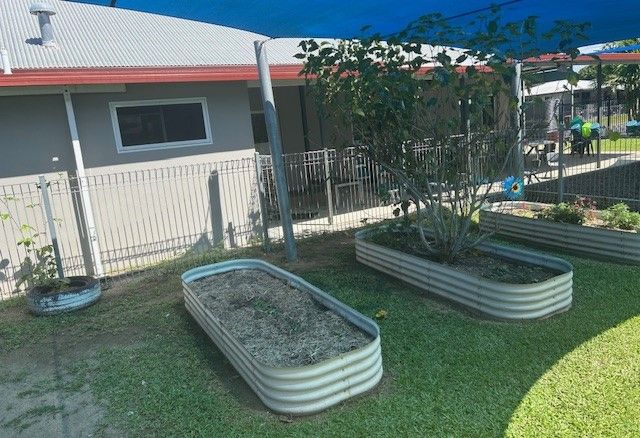 Three metal planters are sitting on top of a lush green lawn in front of a building — Birralee Child Care Centre Assn Inc In Mackay, QLD