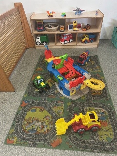 A Toy Garage Is On A Mat On The FloorTable Playing With Toys — Birralee Child Care Centre Assn Inc In Mackay, QLD