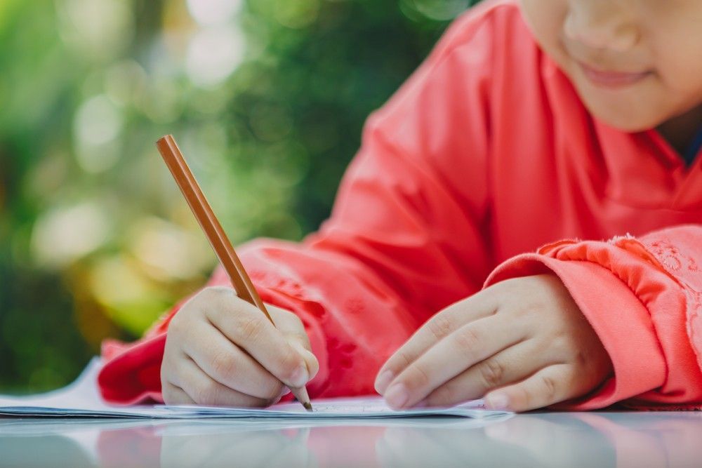 A Young Girl is Writing on a Piece of Paper With a Pencil — Birralee Child Care Centre Assn Inc In Mackay, QLD