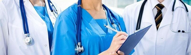 Tres profesionales médicos con uniforme y bata, cada uno con un estetoscopio. Uno sostiene un portapapeles.