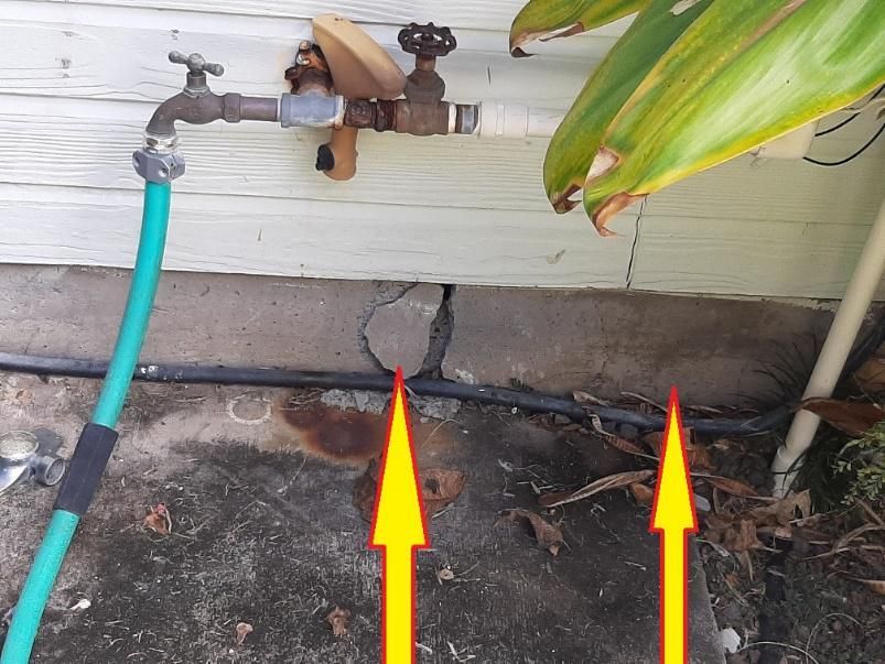 A green hose is attached to a faucet on the side of a house