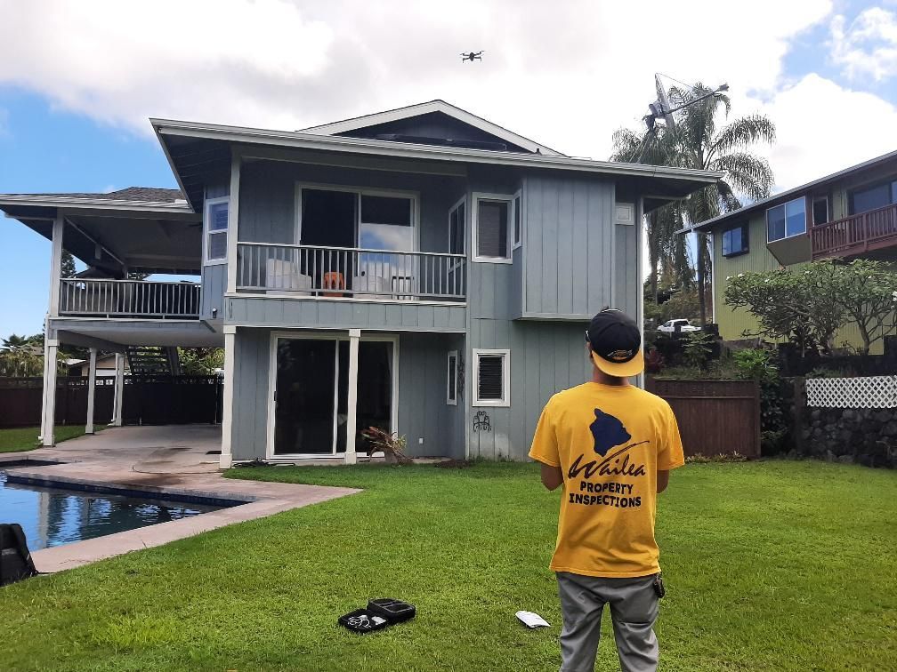 A man in a yellow shirt is standing in front of a large house.
