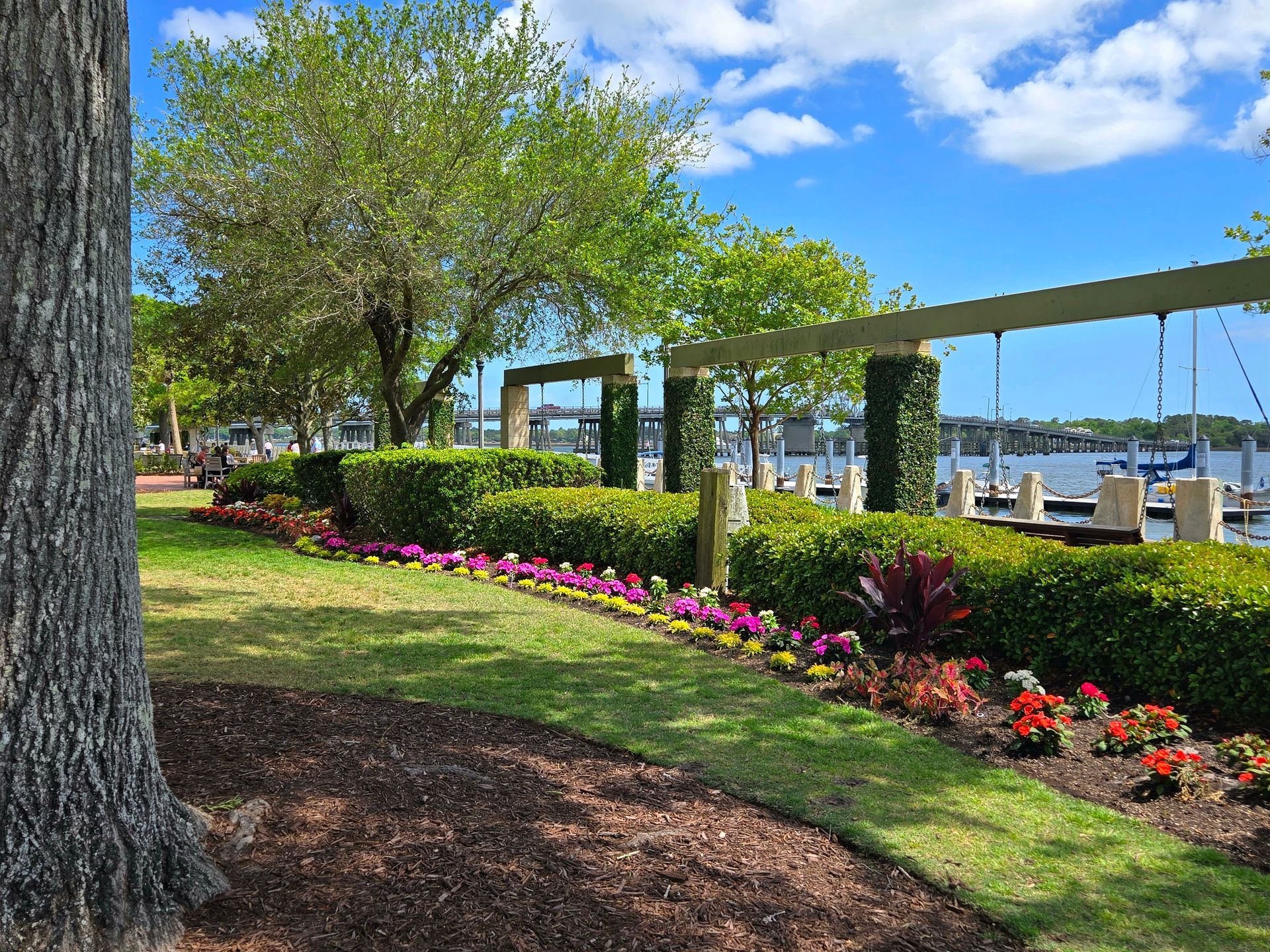 Beaufort SC waterfront park with trimmed hedges, colorful flowers, and a waterfront view under a blue sky.