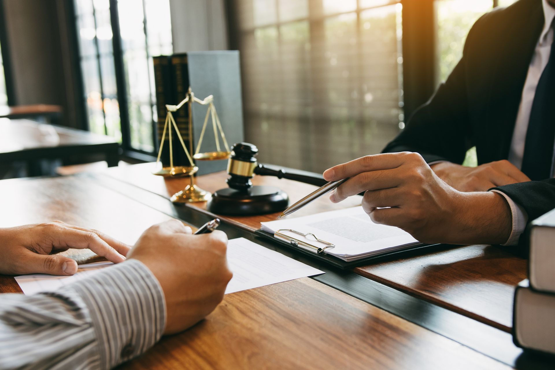 Lawyer and client signing documents at a desk with gavel and scales of justice