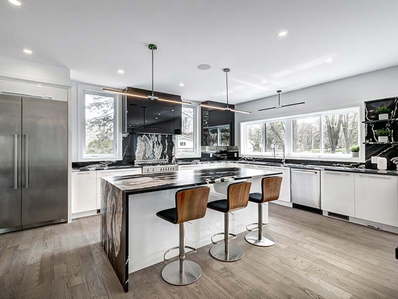 A kitchen with a large island , stools and a refrigerator.