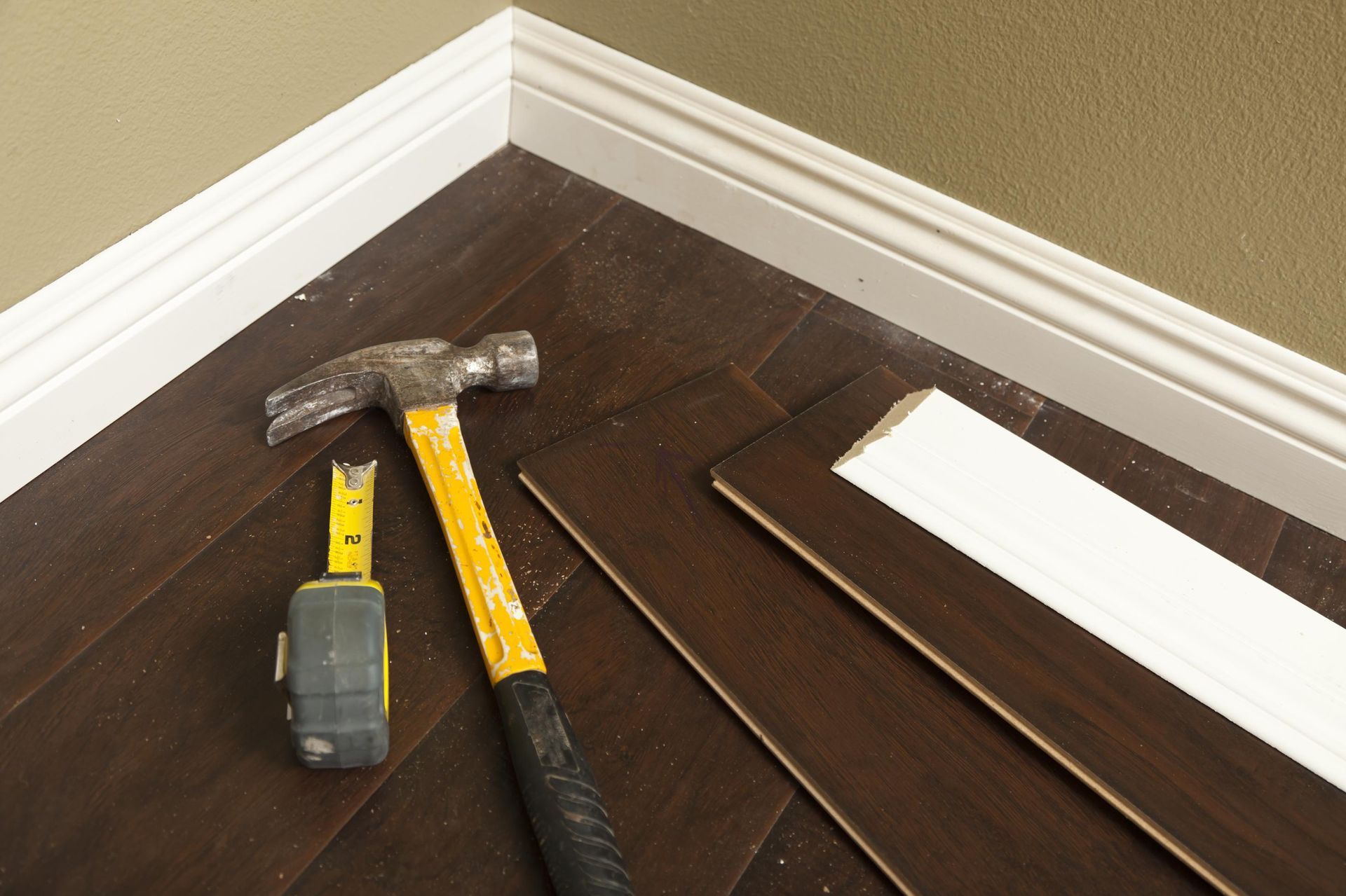 A hammer and tape measure are on a wooden floor.