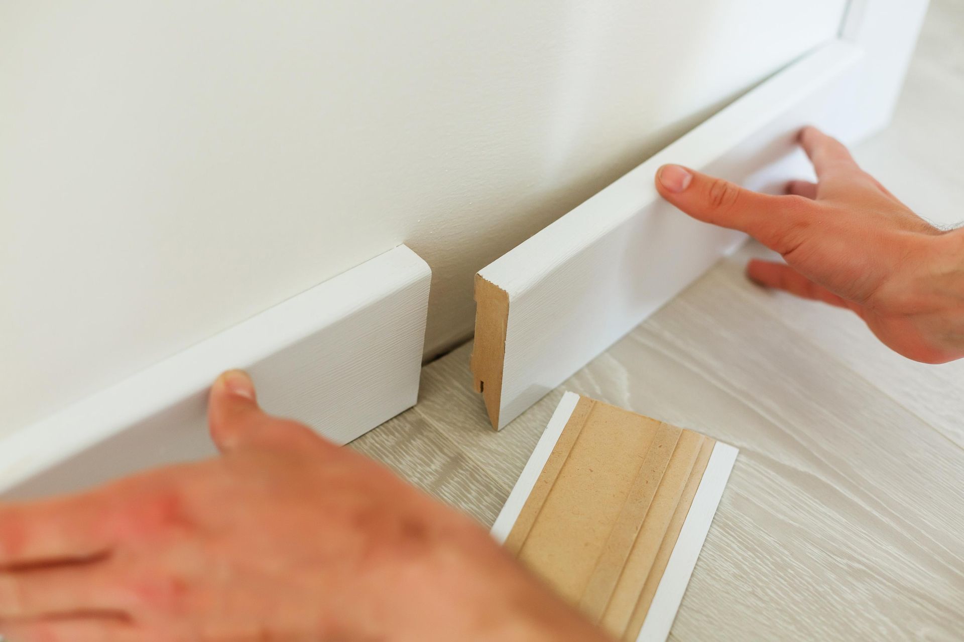 A person is installing a white skirting board on a wall.