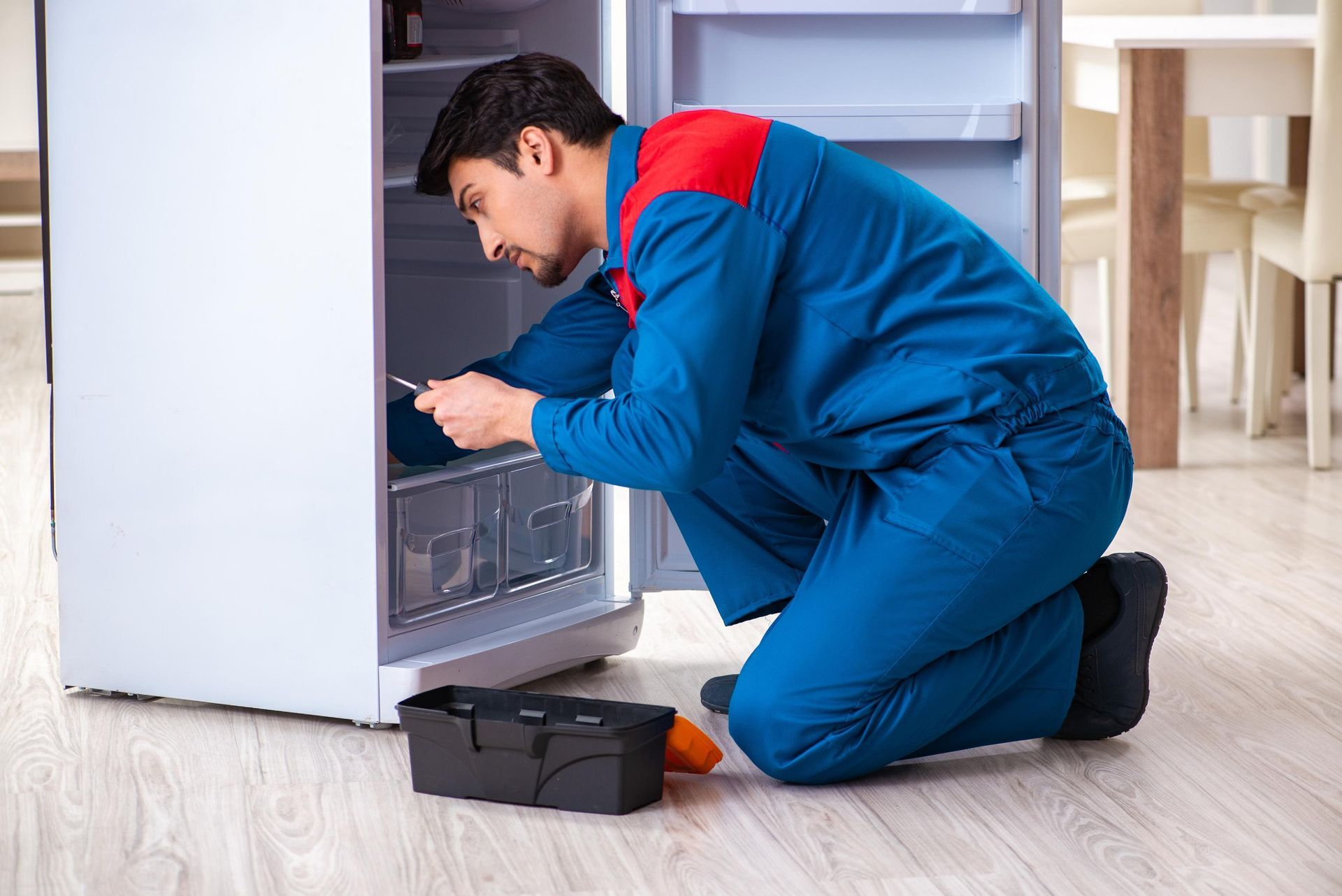 A man is repairing a refrigerator in a kitchen.