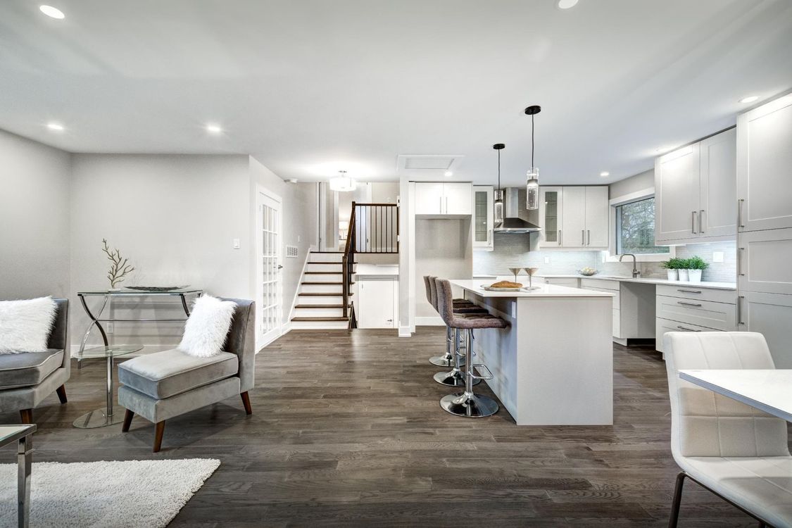 A living room and kitchen in a house with hardwood floors and white cabinets.