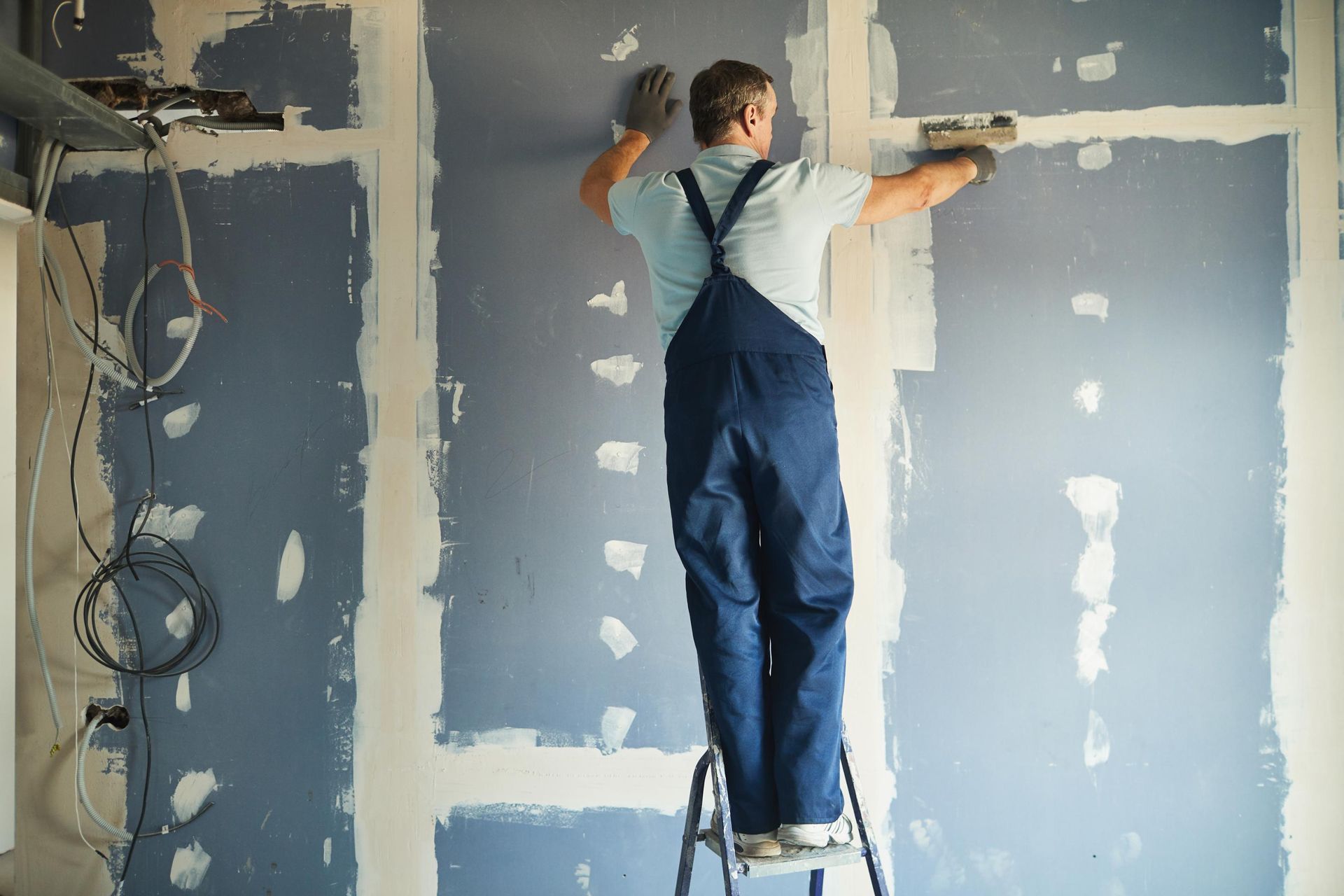 A man is standing on a ladder and plastering a wall.