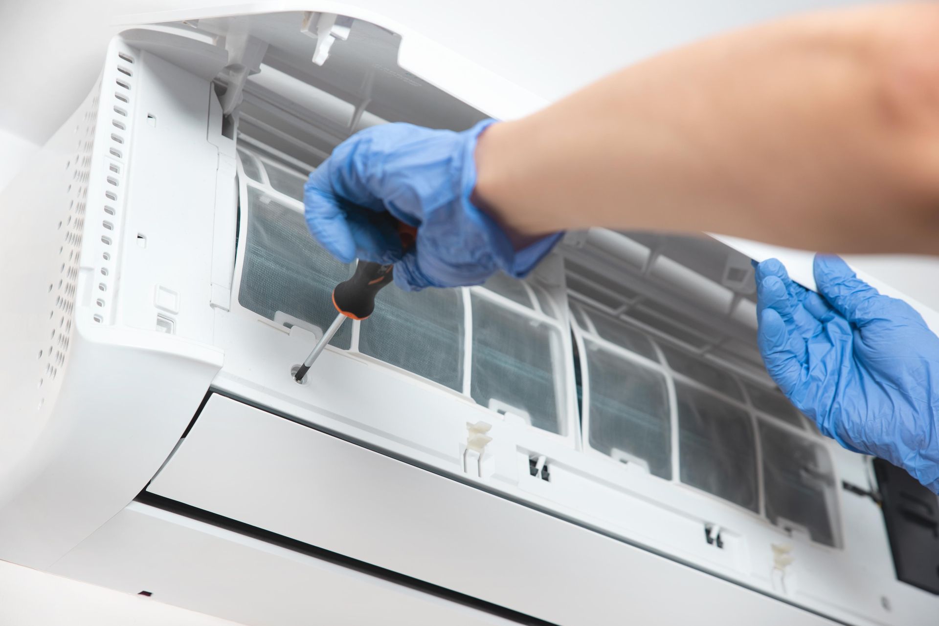 A person wearing blue gloves is fixing an air conditioner with a screwdriver.