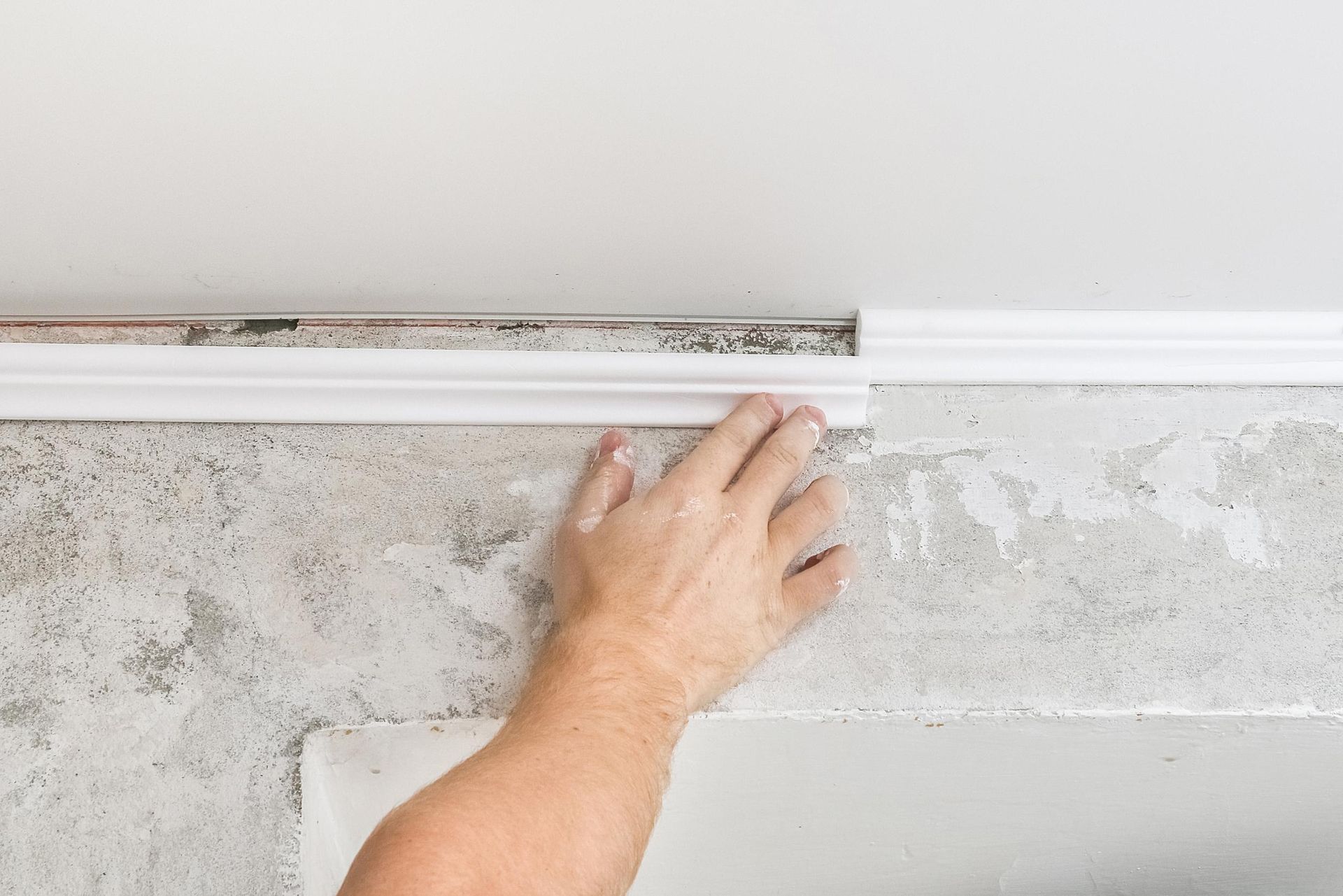 A person is installing molding on a ceiling.