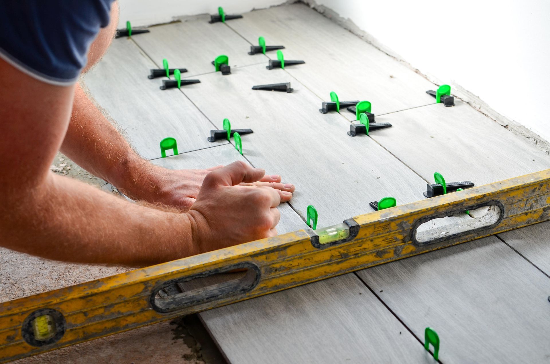 A man is using a level to level a tile floor.