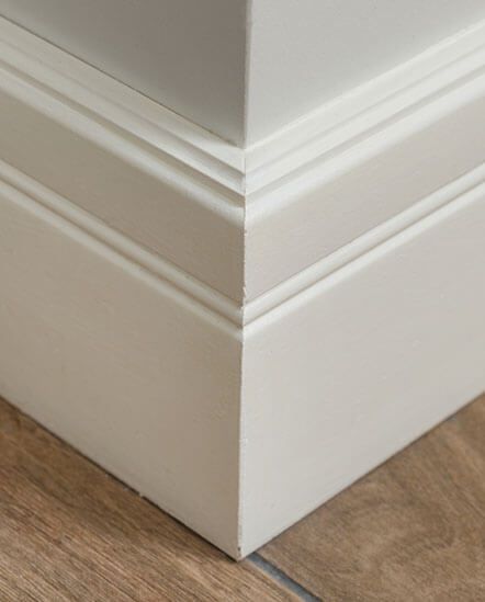 A close up of a white skirting board on a wooden floor.