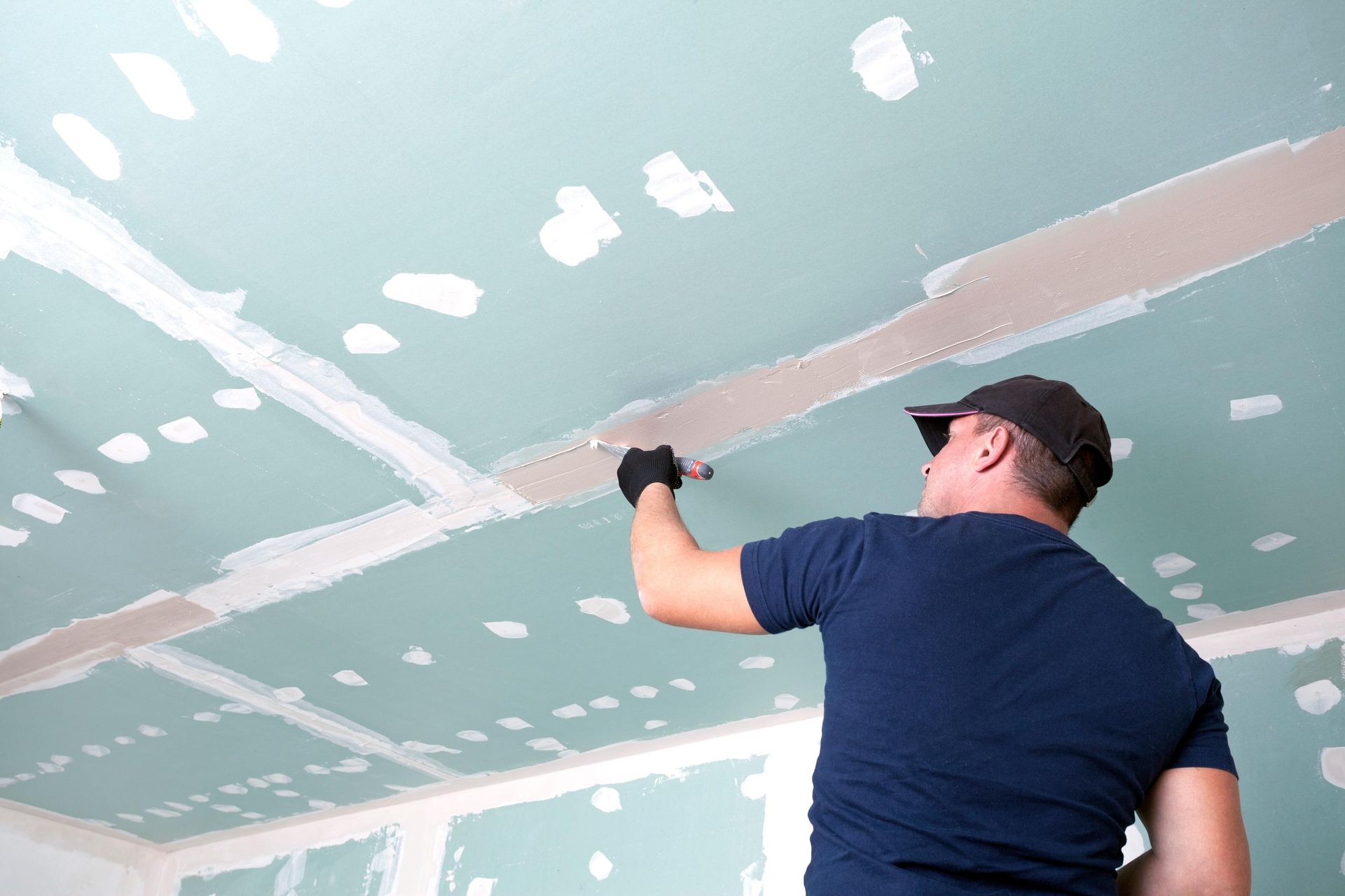 A man is plastering a ceiling in a room.