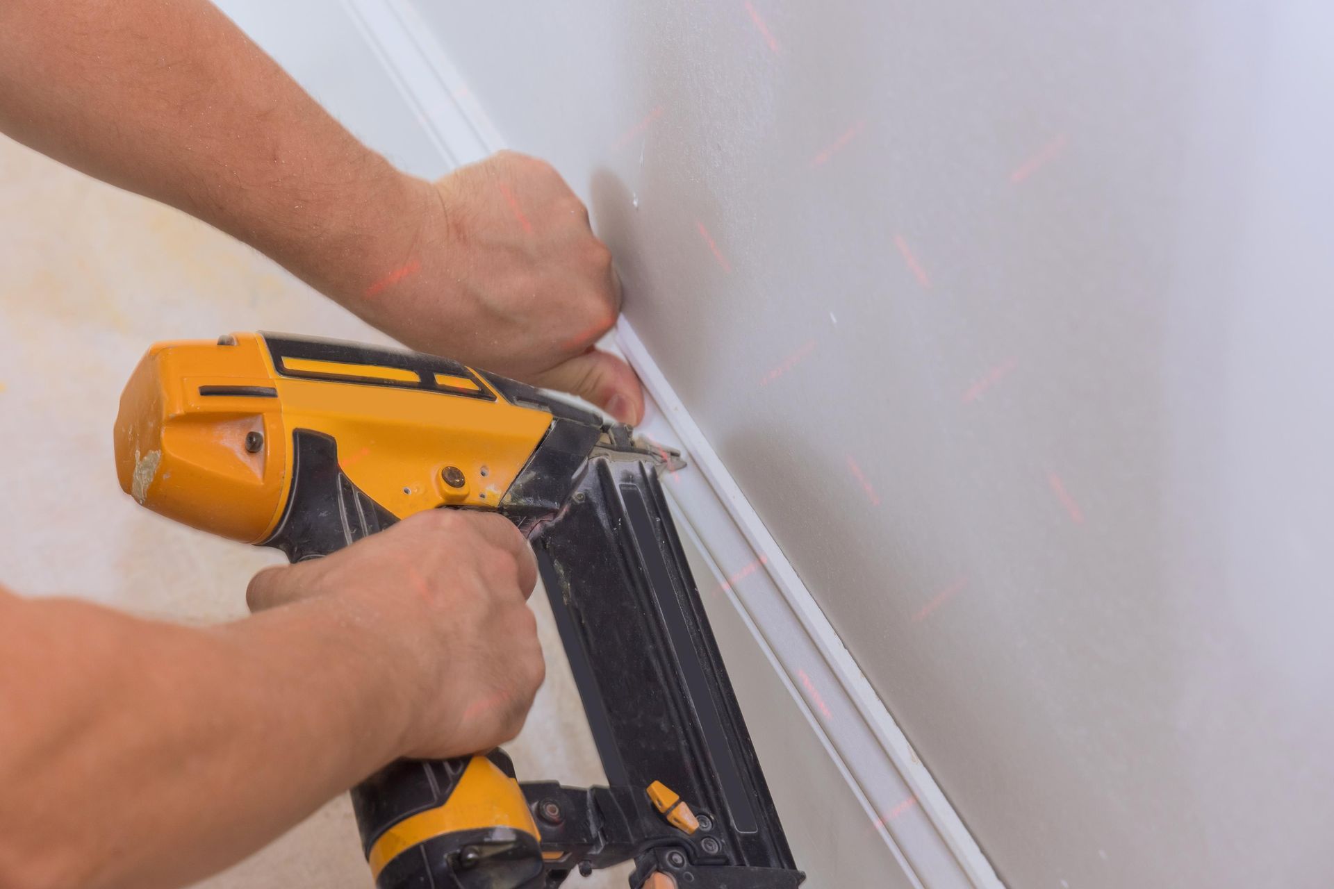 Carpenter using a brad nail gun to nailing base molding trim for works new home.