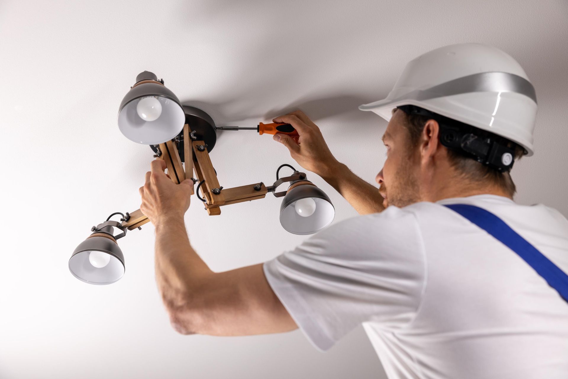 A man is fixing a lamp on the ceiling with a screwdriver.