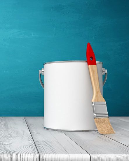 A can of paint and a brush on a wooden table.