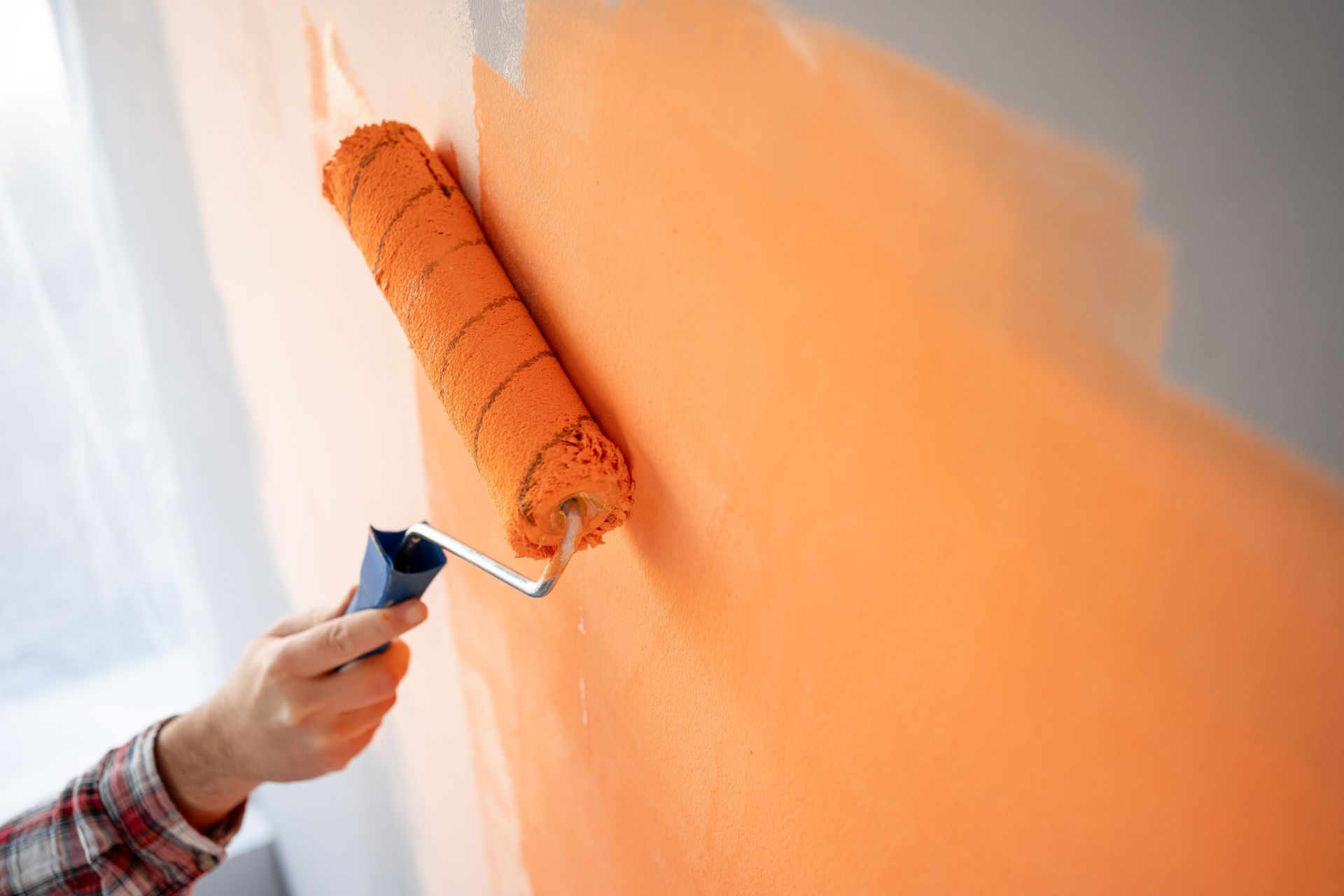 A person is painting a wall with an orange paint roller.