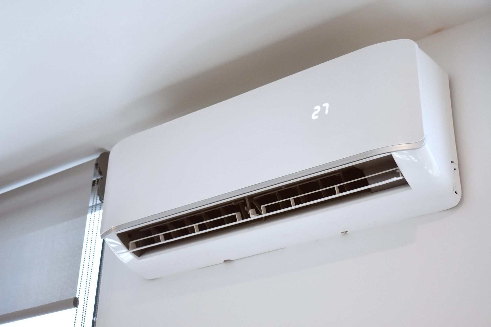 A white air conditioner is hanging on a wall next to a window.