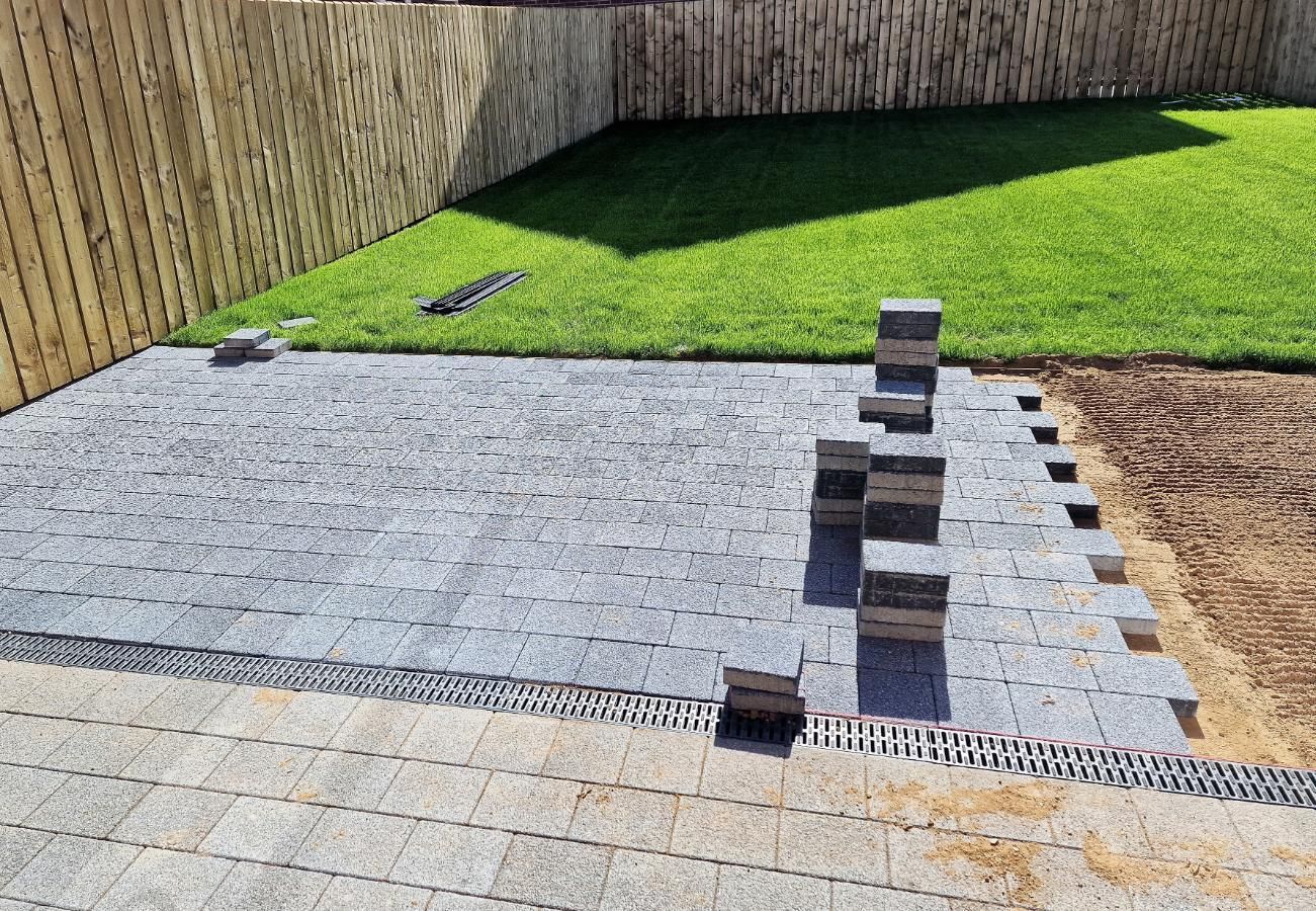 A patio is being built in a backyard next to a lush green lawn.