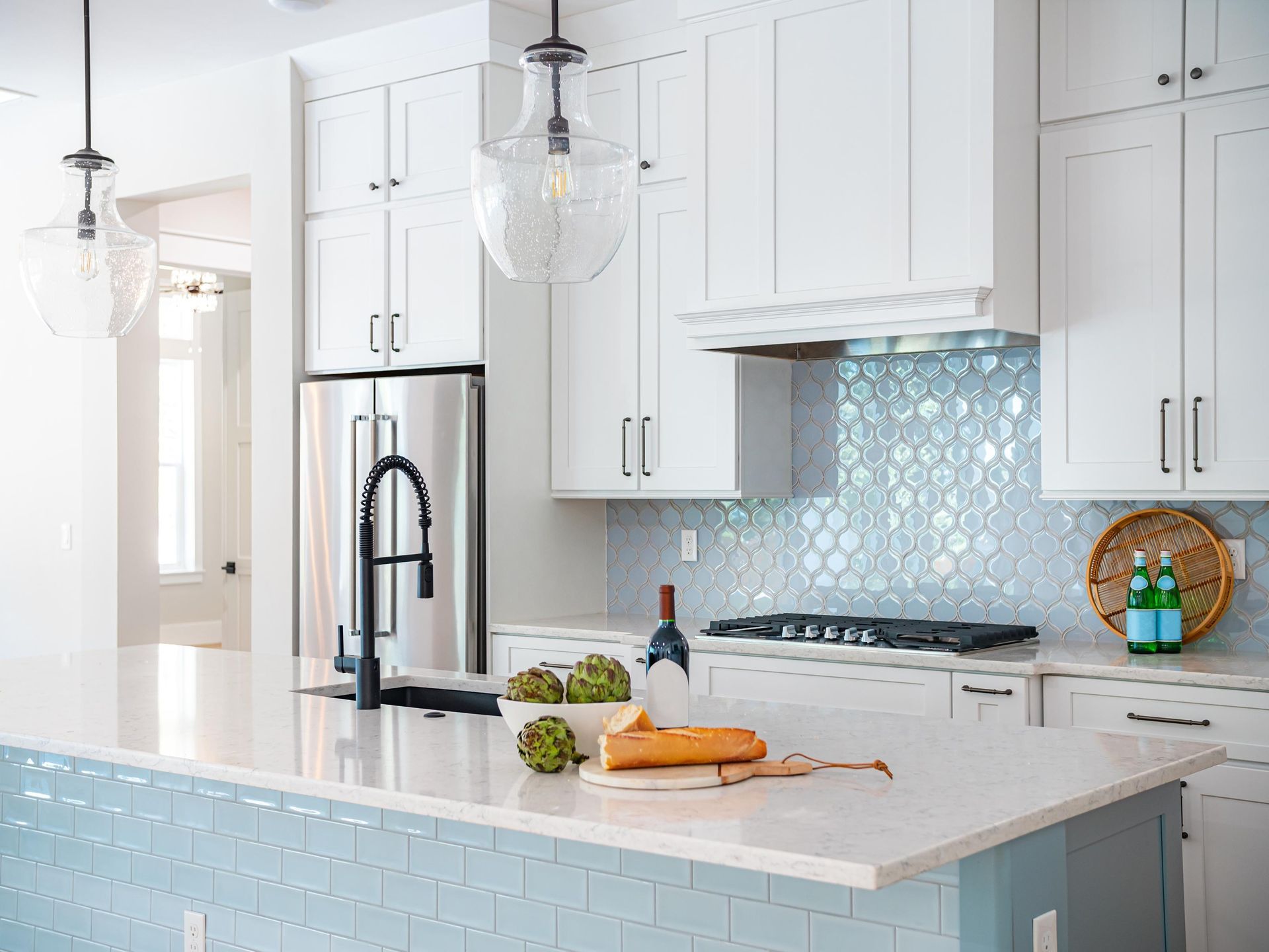 A kitchen with white cabinets, blue tiles, stainless steel appliances ,and a large island.