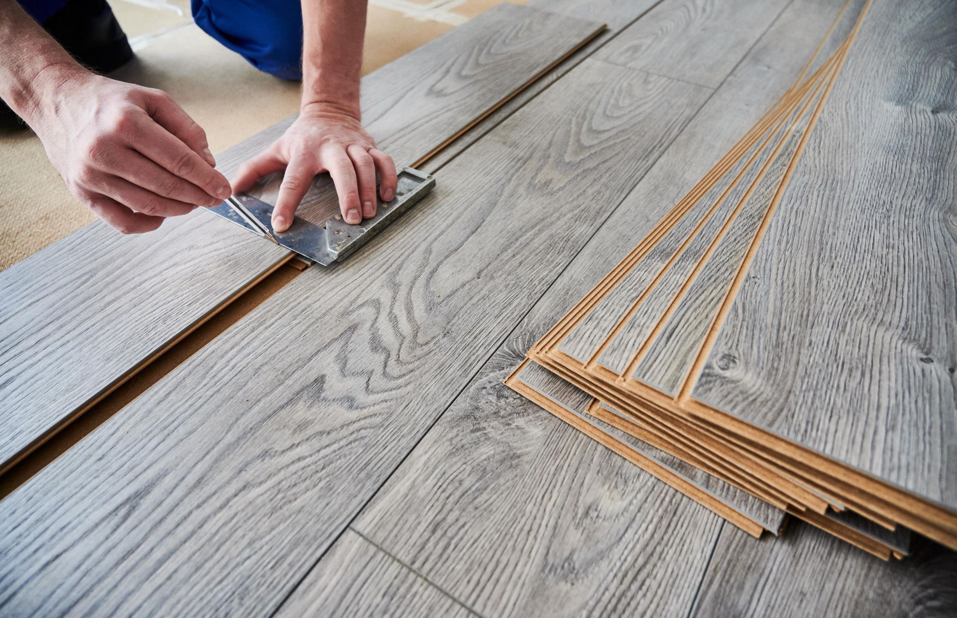 A person is installing a wooden floor with a spatula.