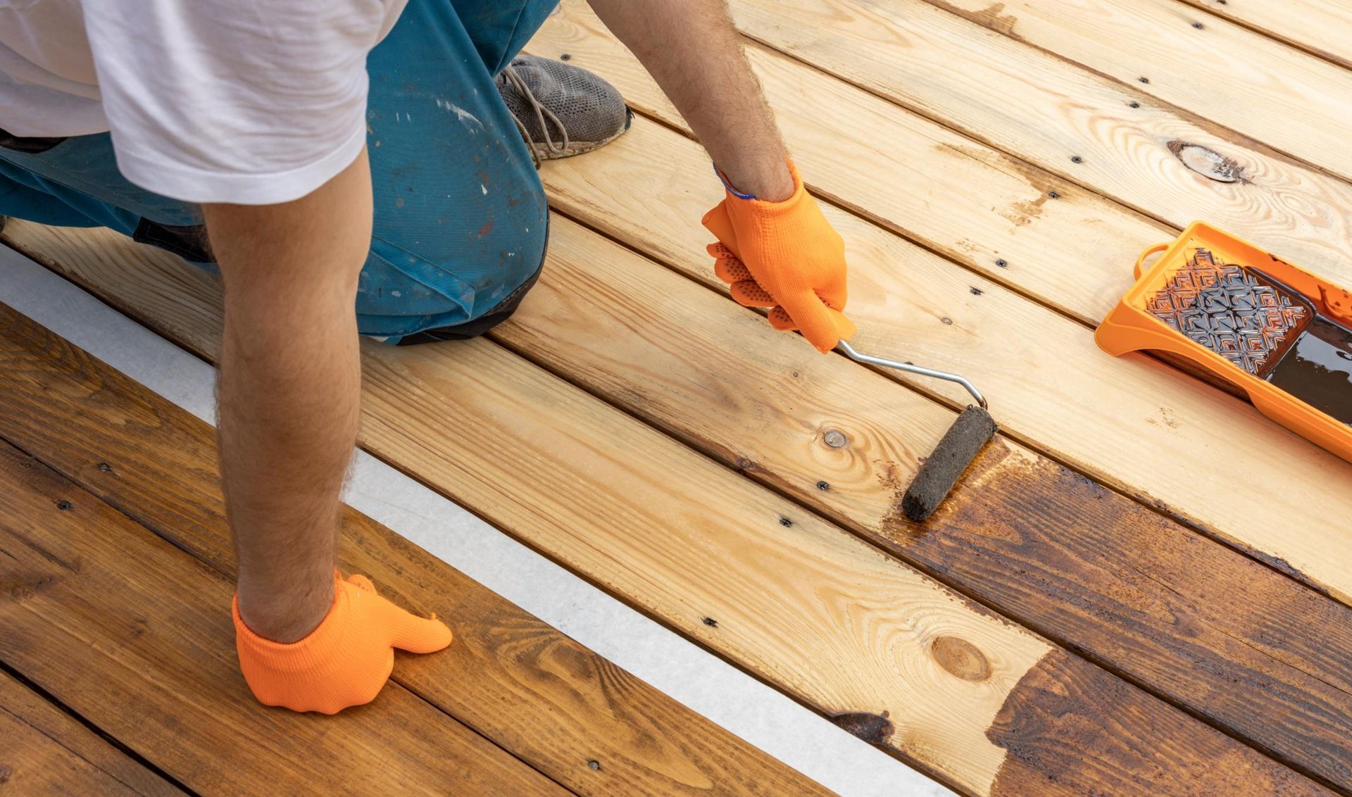 A person is painting a wooden deck with a roller.