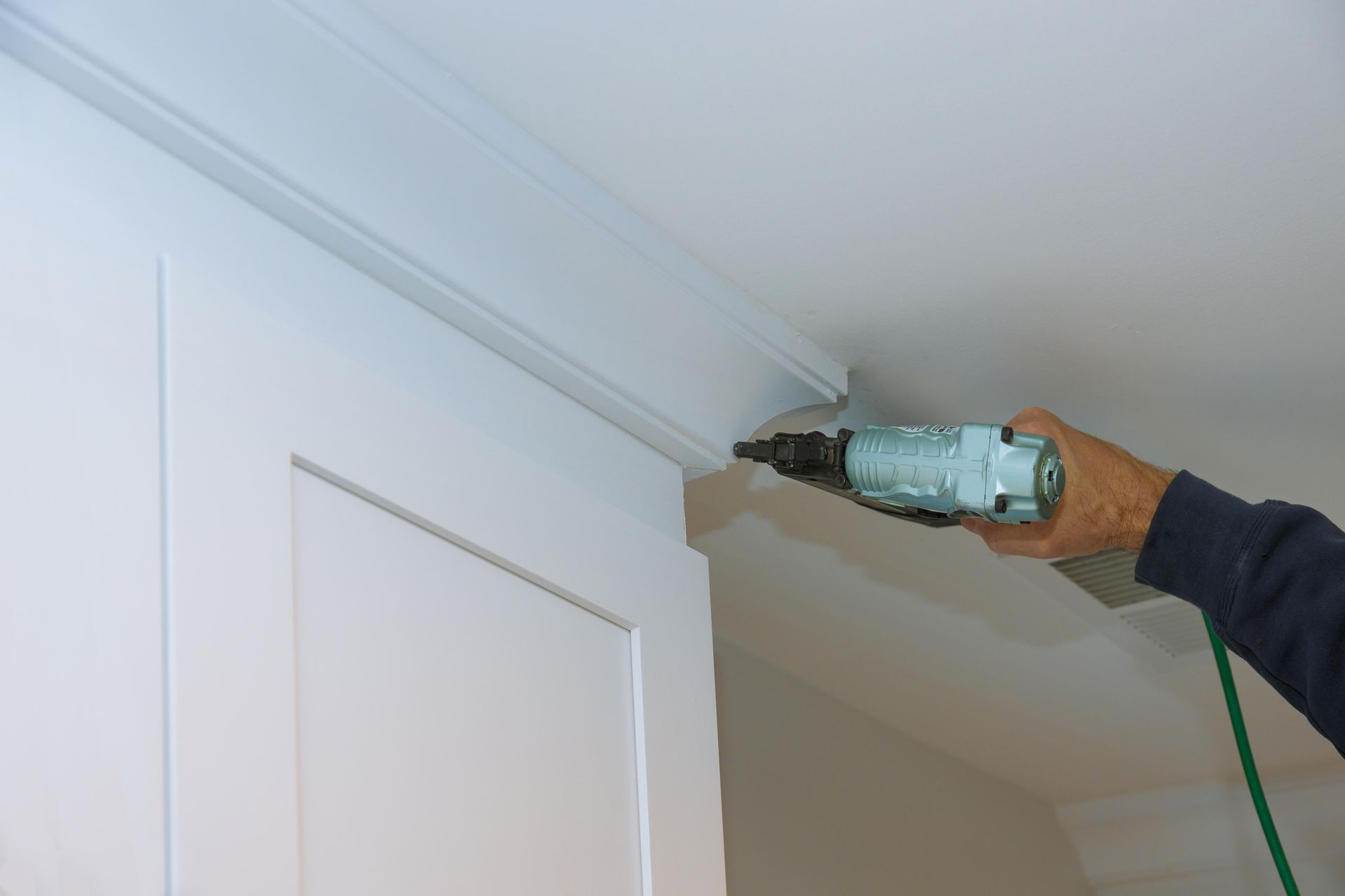 A person is using a drill to install molding on a wall.