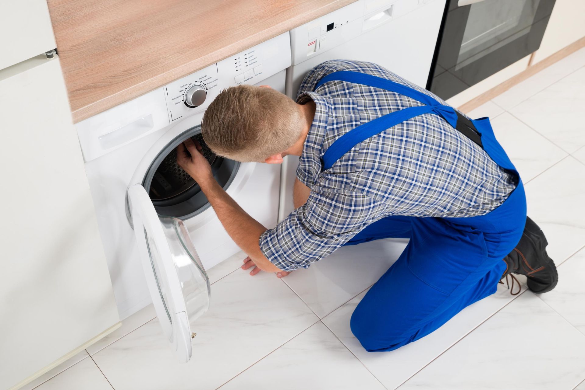 A man is fixing a washing machine in a kitchen.