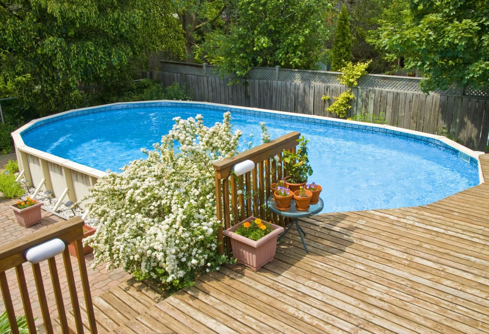 A large swimming pool is surrounded by potted plants and a wooden deck.