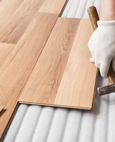 A person is installing a wooden floor with a hammer.