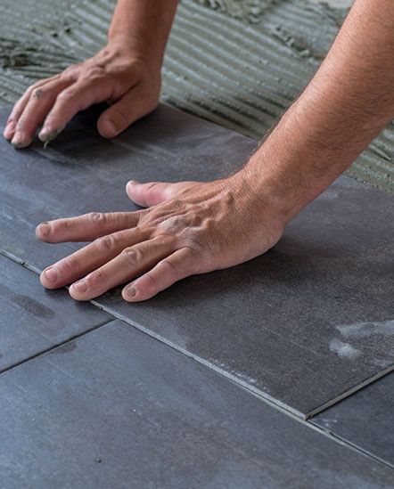 A person is laying tiles on the floor with their hands.