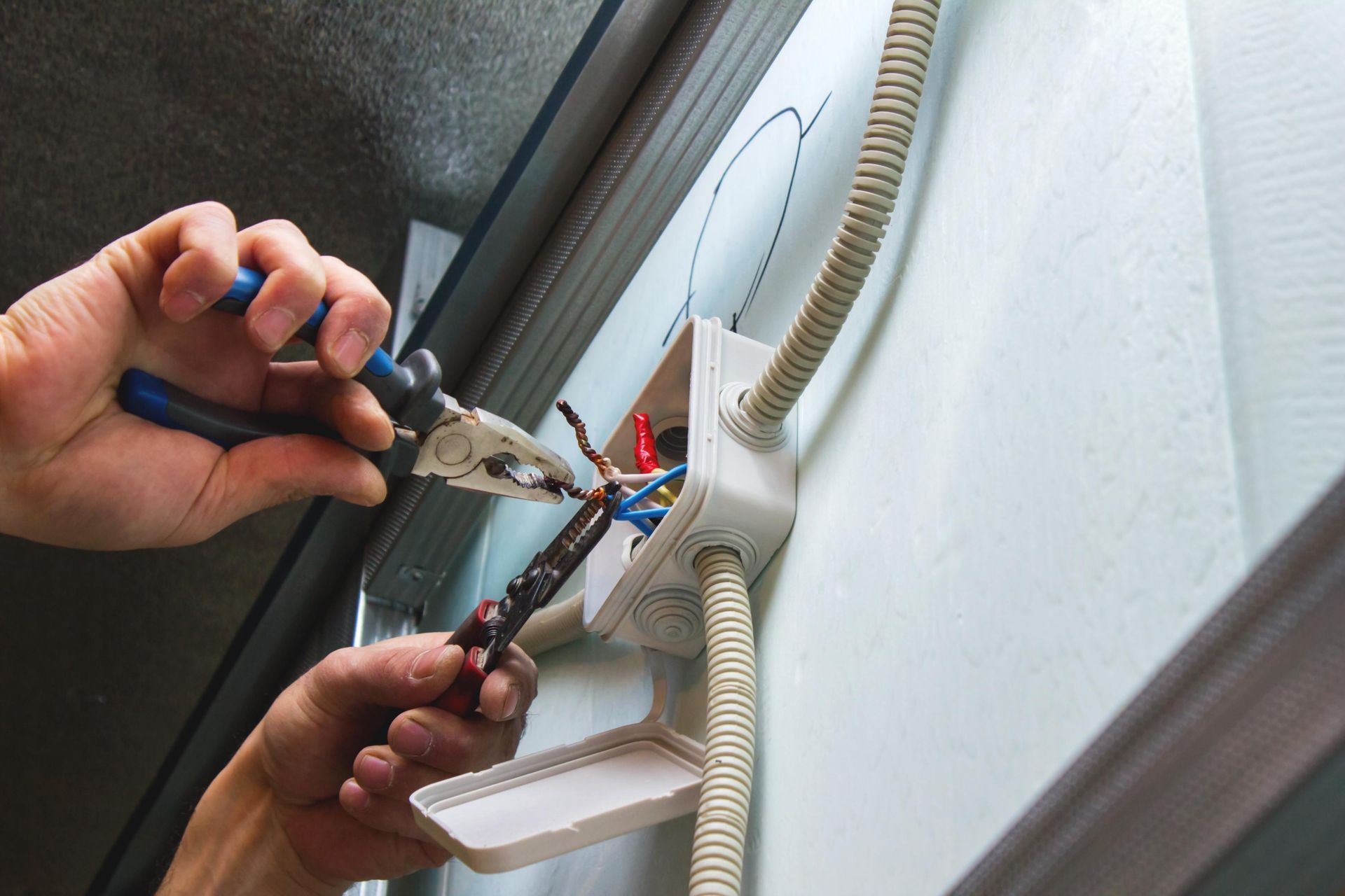 A person is working on an electrical box with pliers.