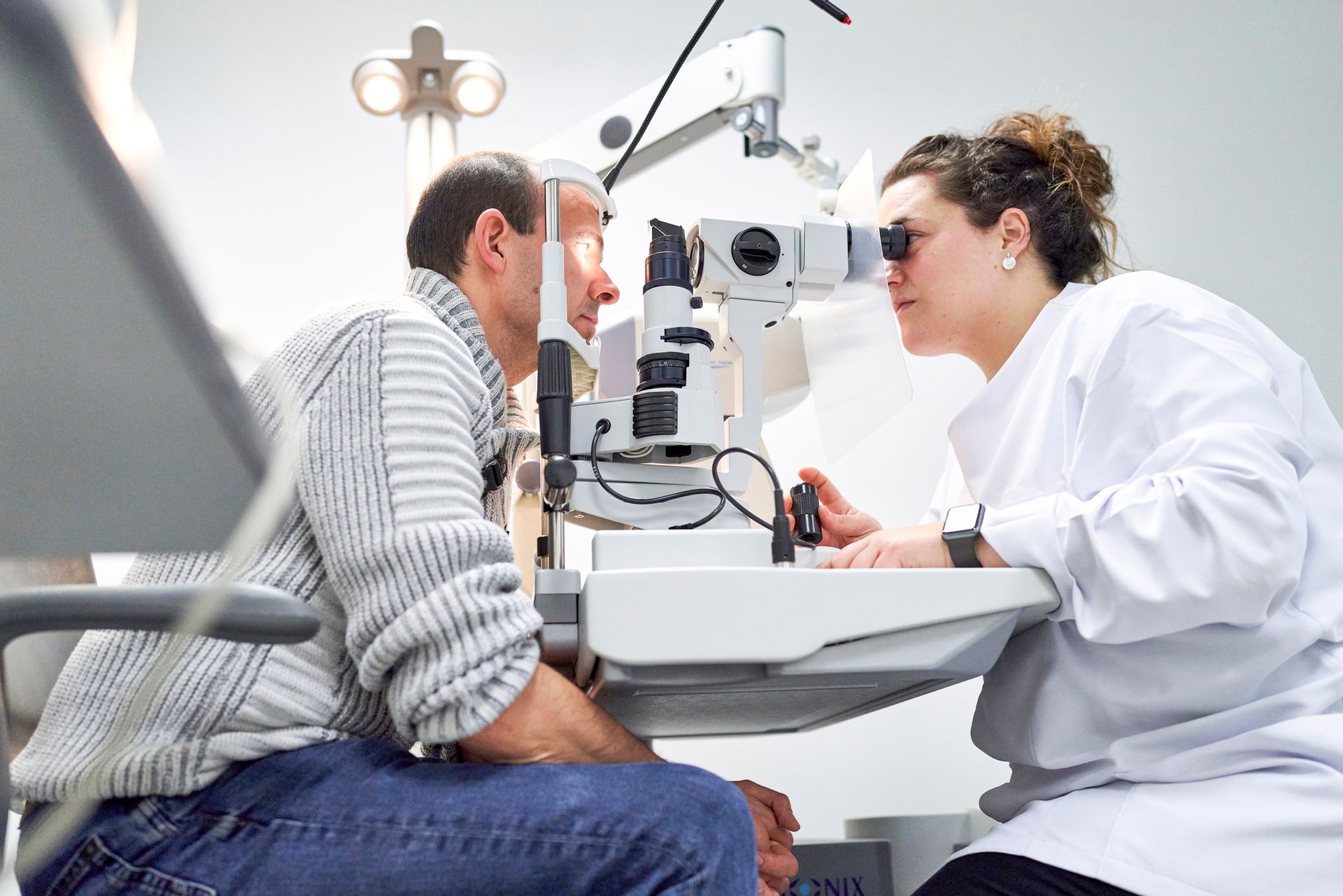 An eye doctor performing an eye exam on a patient, using a phoropter and other examination tools.