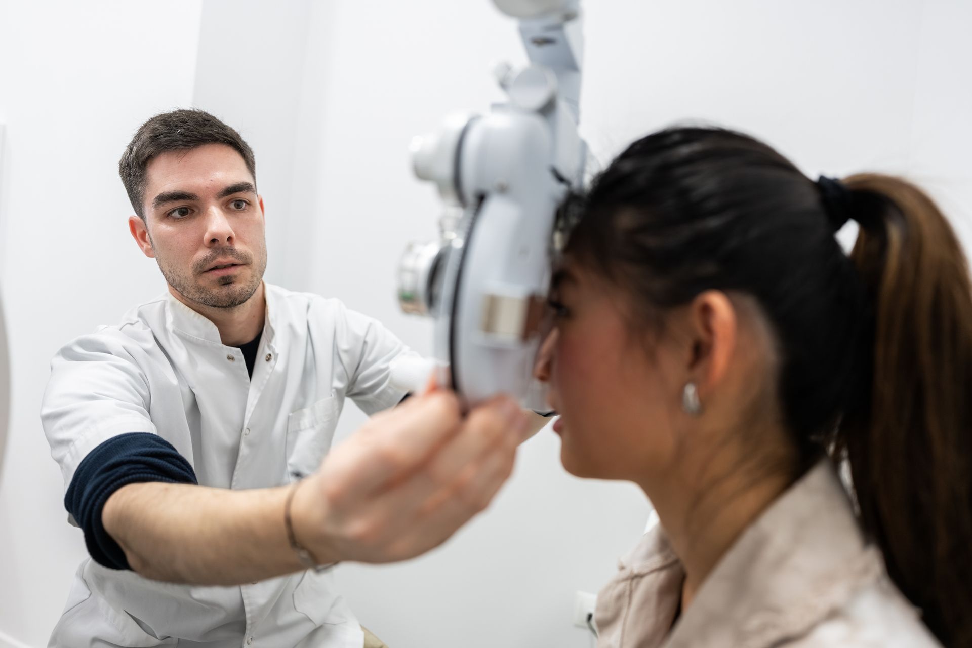 A male eye doctor checks a patient's eye using an examination tool in a medical office. A male eye doctor checks a patient's eye using an examination tool in a medical office.