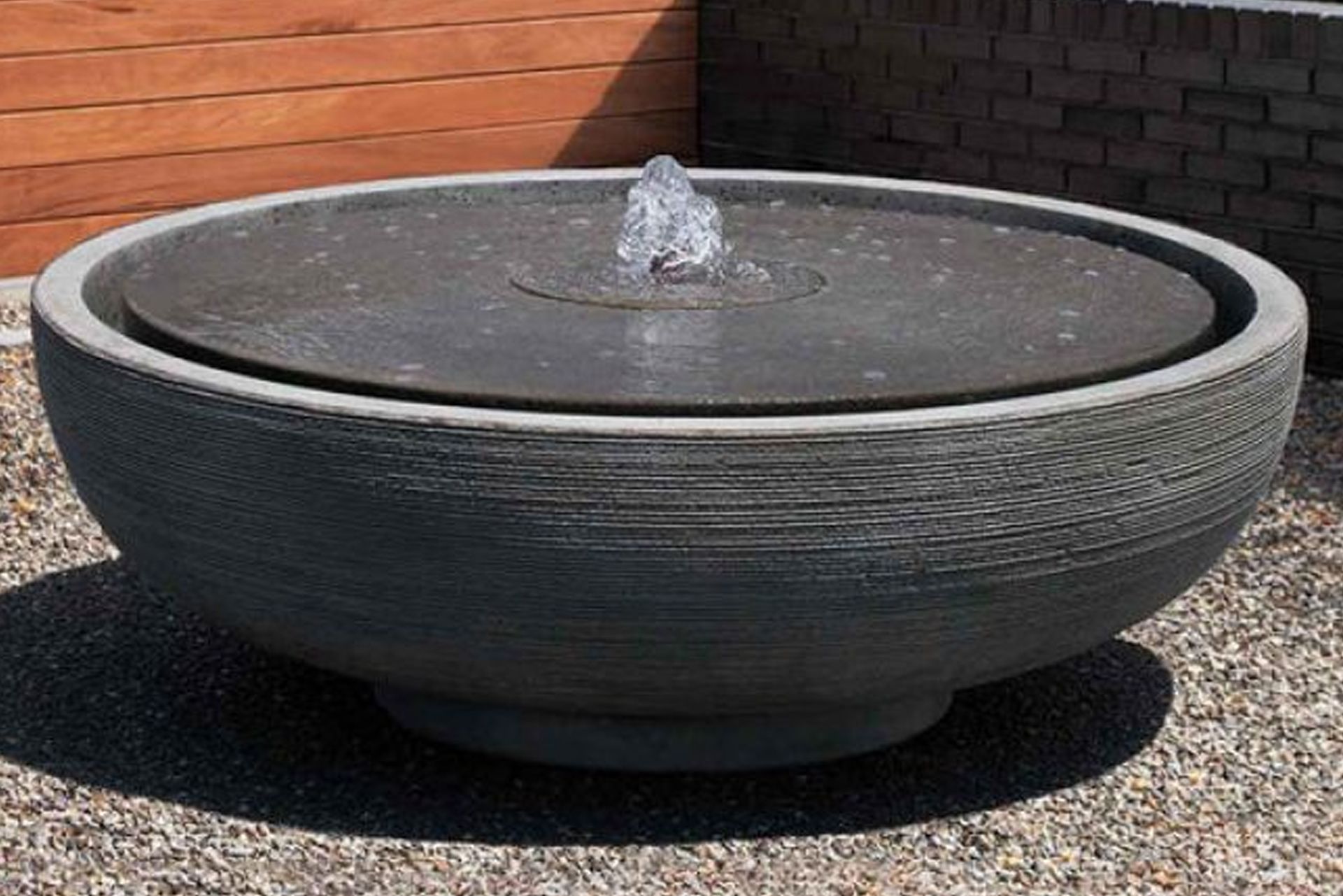 Rectangular water fountain with a statue, surrounded by trees and gravel patio.