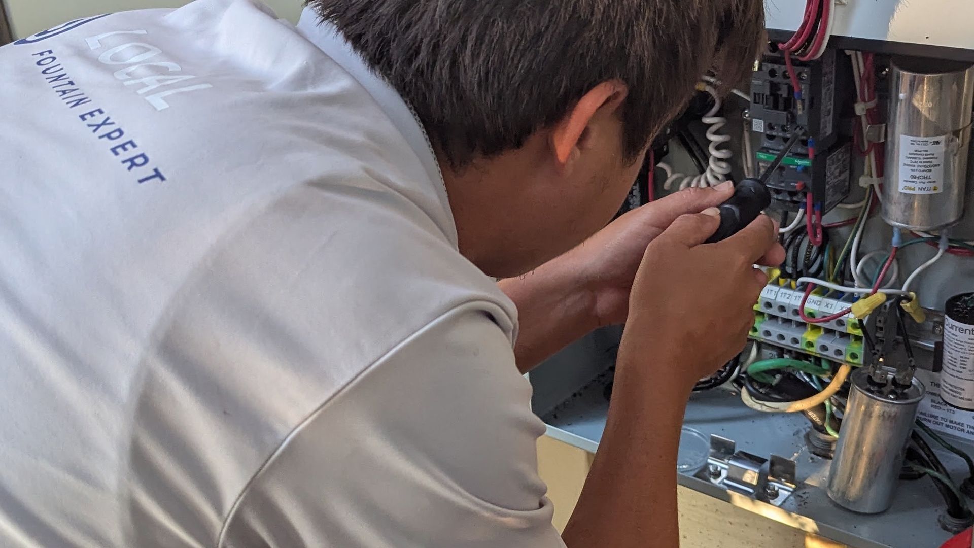 Man in a white shirt working on electrical wiring in an outdoor setting.