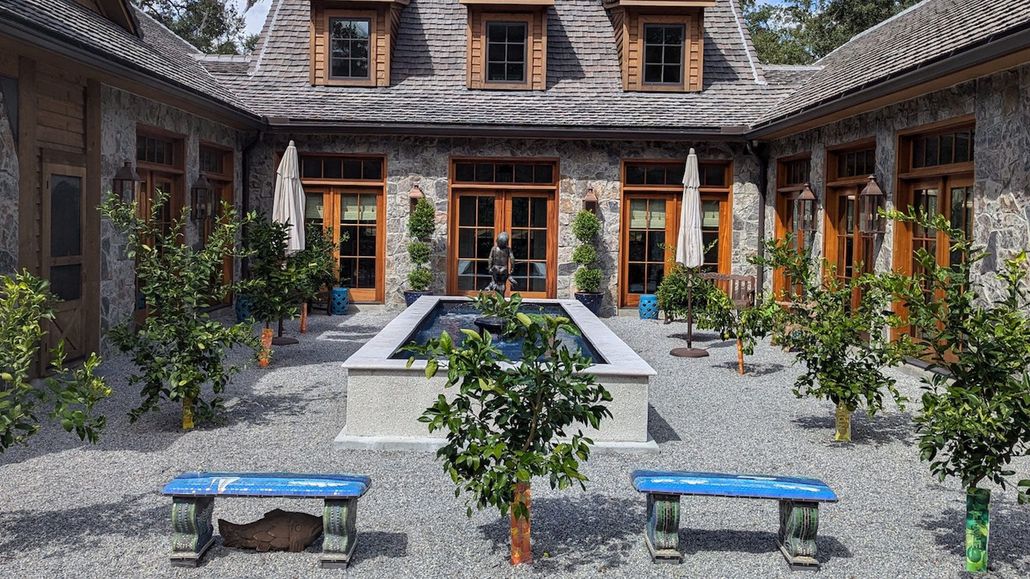 Ornate tiered fountain on green lawn with trees and parked vehicle.
